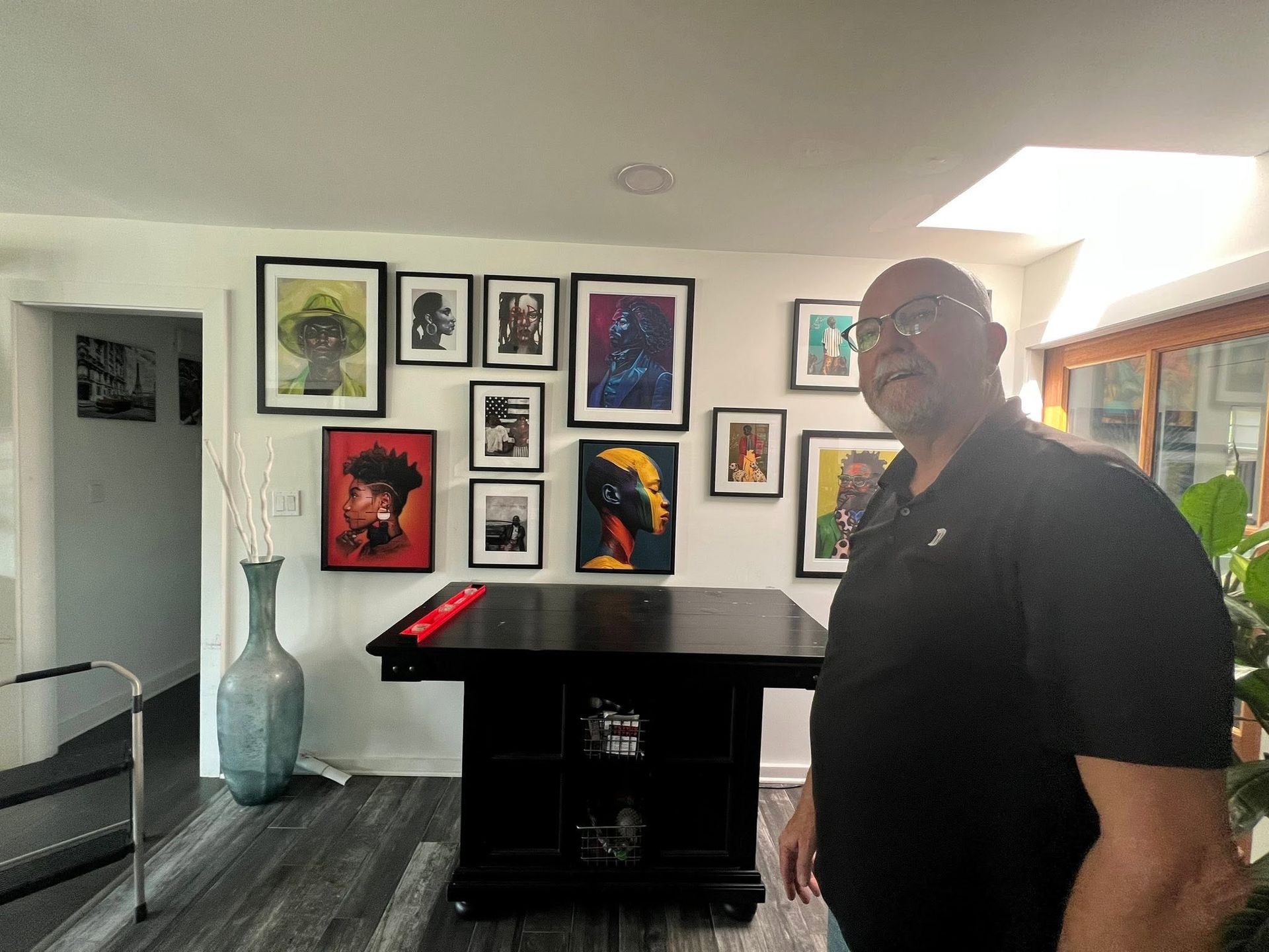 Person standing in a bright living room with framed art wall and large vase