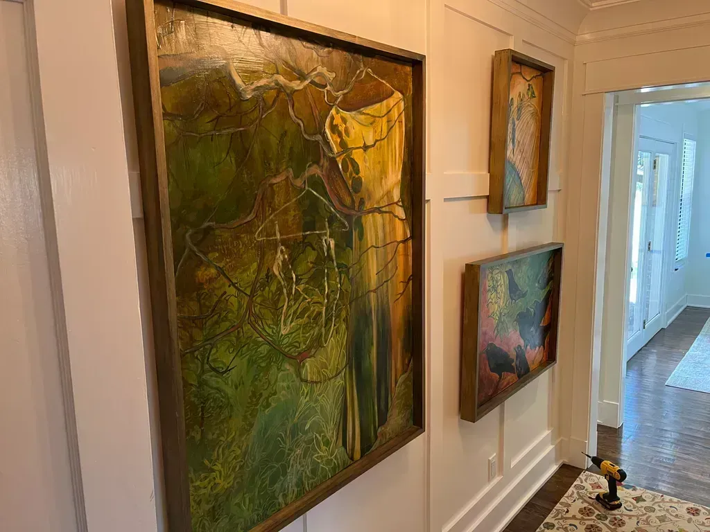 Hallway with three framed abstract paintings in earthy green, gold, and blue tones on white walls