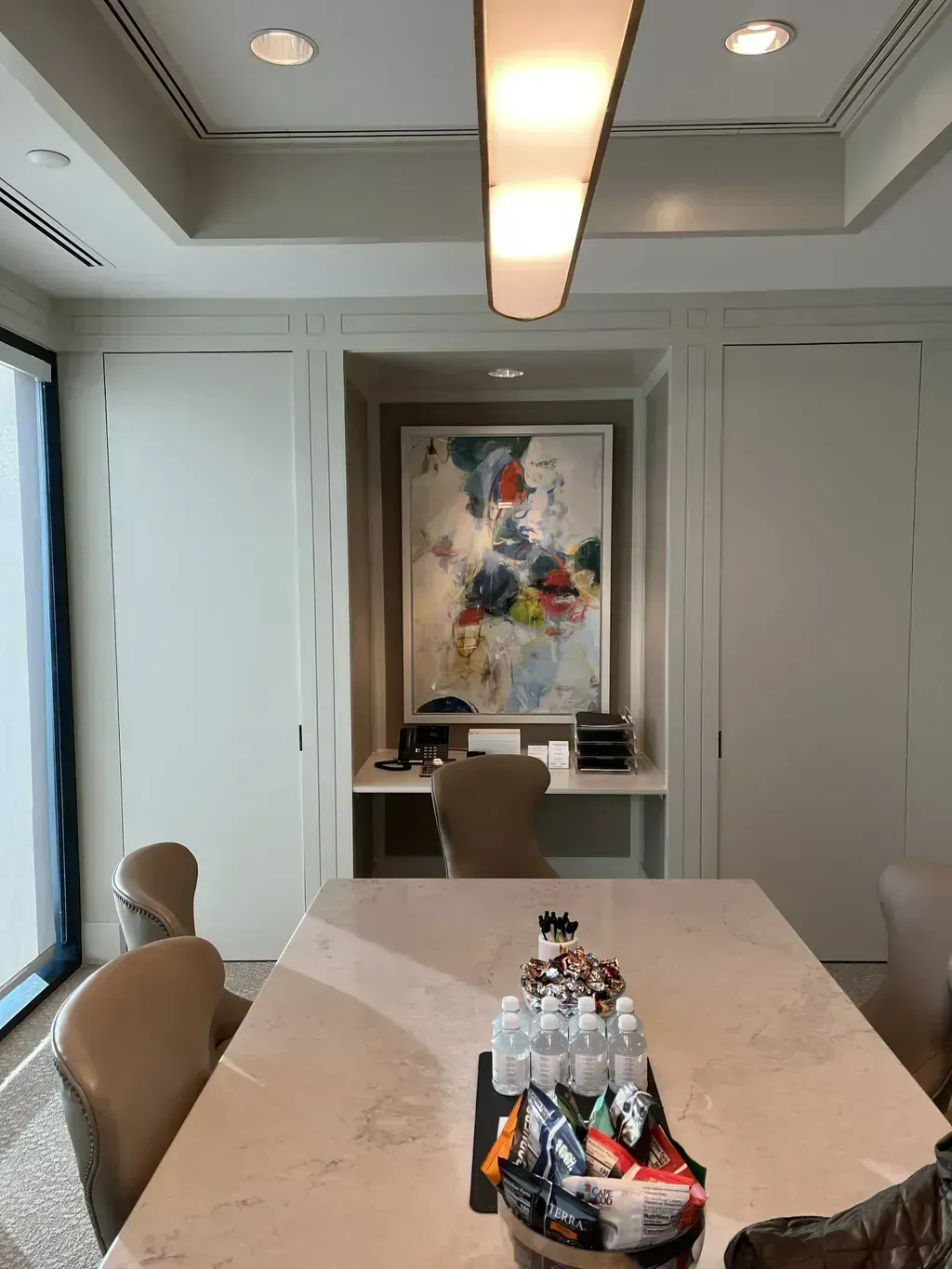 Modern conference room with long table, beige chairs, water bottles, and abstract wall art.