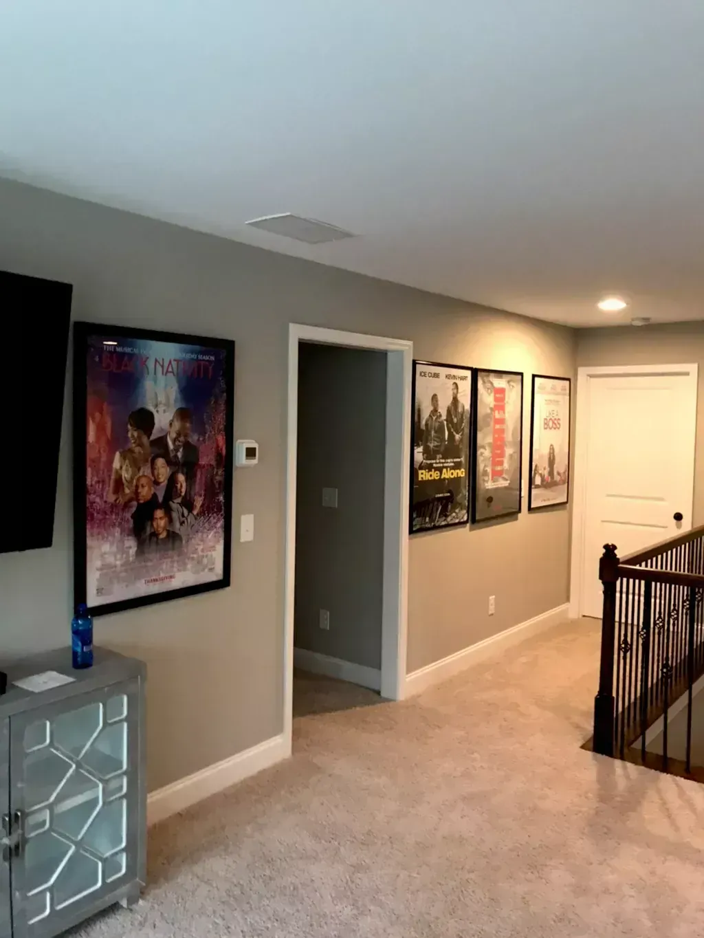 Hallway with movie posters, beige carpet, gray walls, and white doors near a staircase.