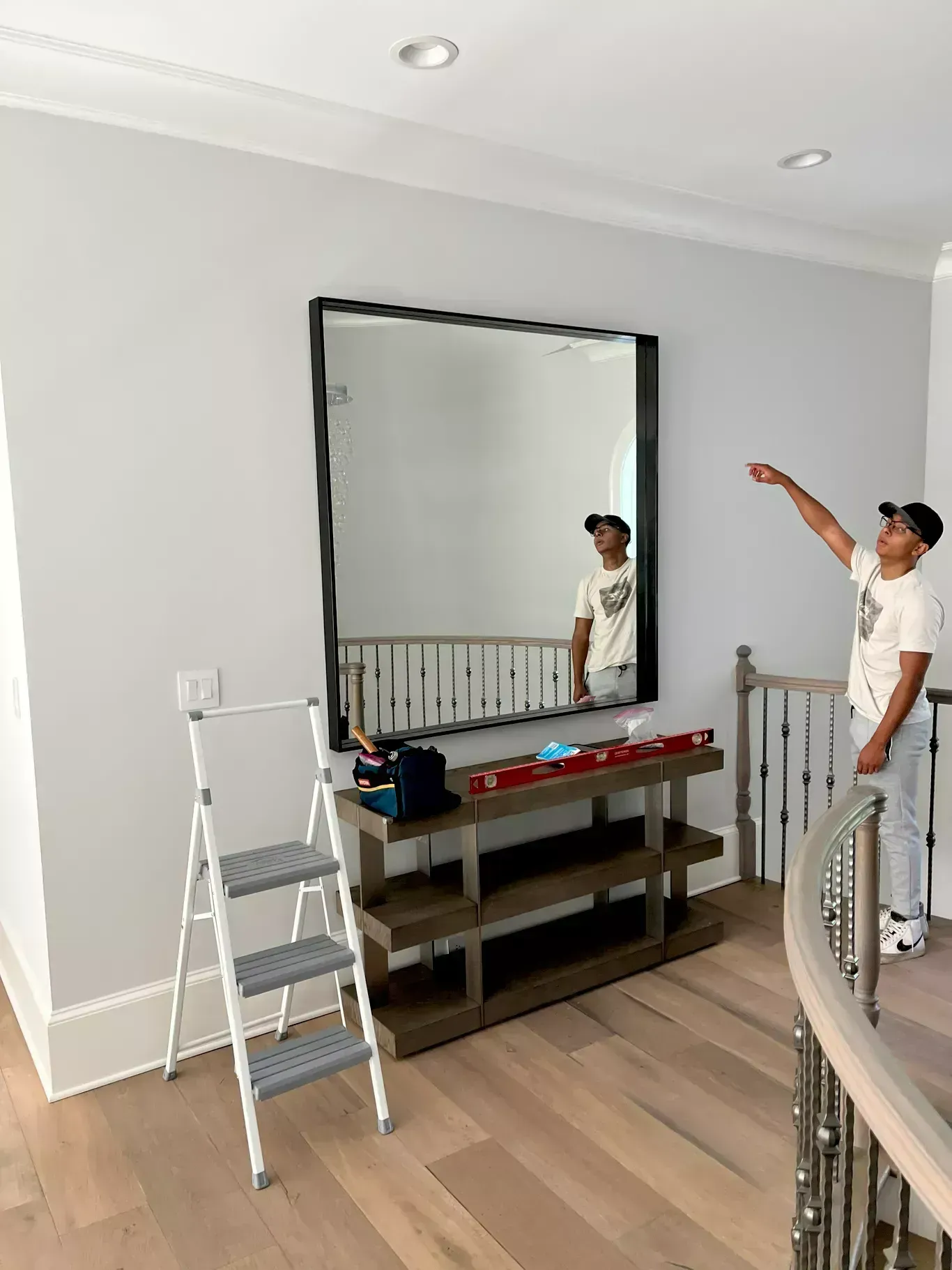 Person pointing at a large wall mirror in a bright room with a ladder and console table