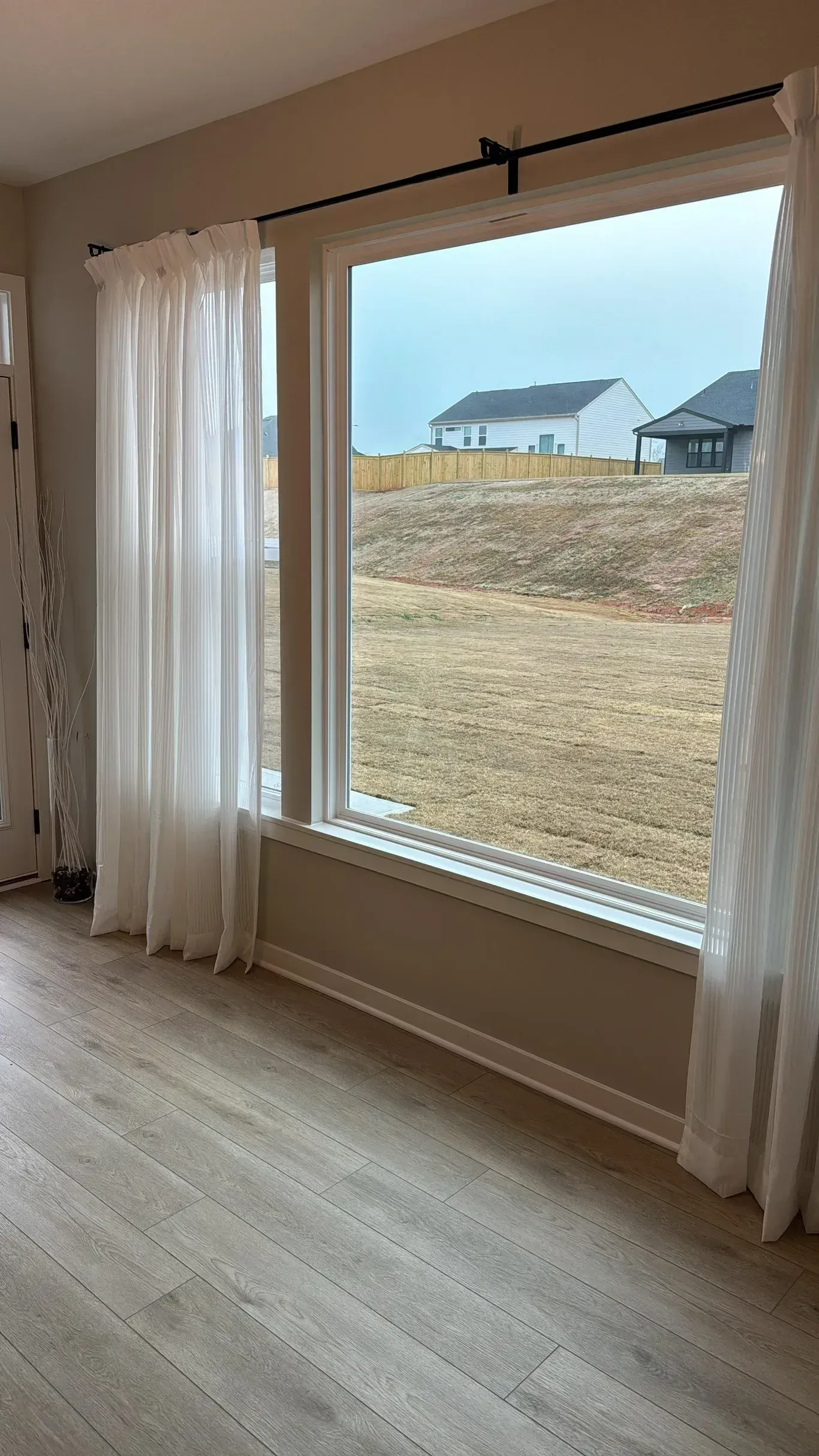 Large window with sheer white curtains overlooking a grassy yard and a small pavilion outside