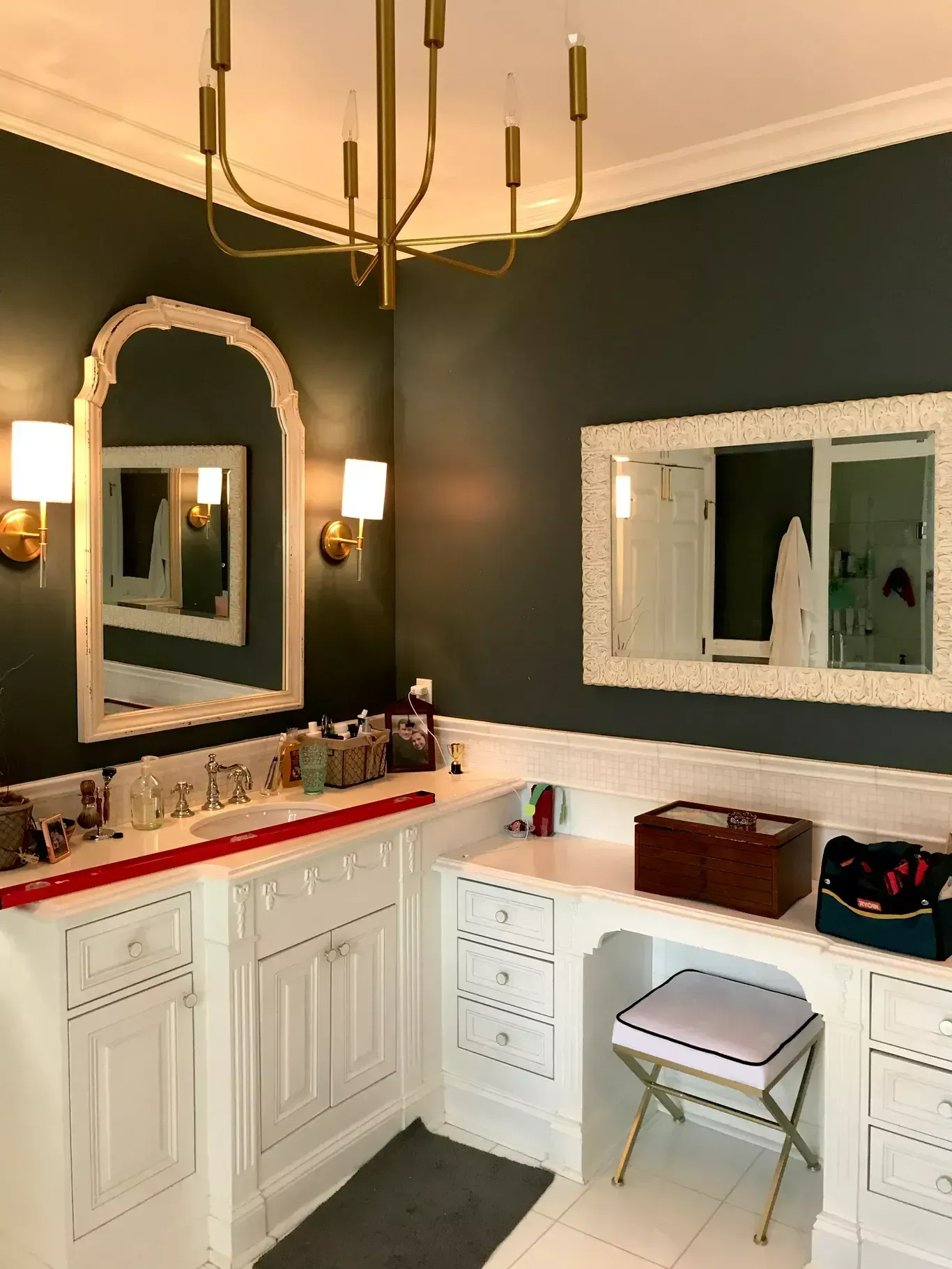 Modern bathroom with dark walls, white cabinets, red countertop, mirrors, and a gold chandelier