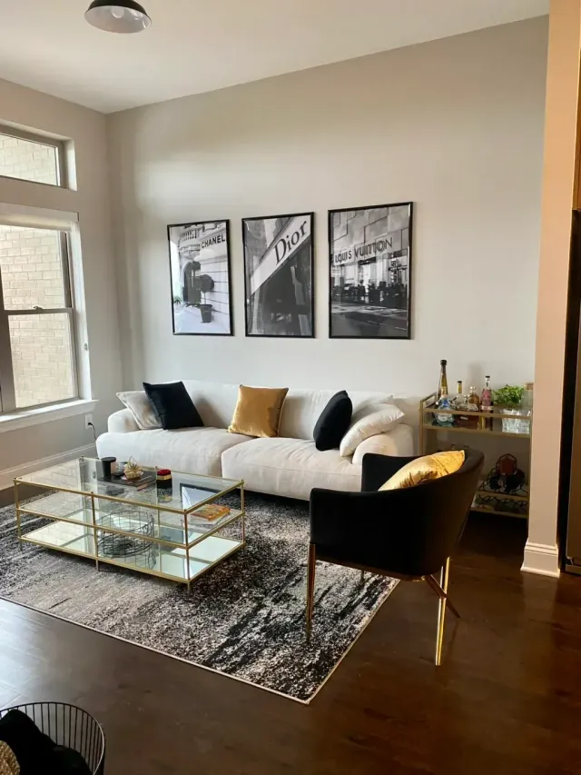 Modern living room with white sofa, glass coffee table, black chair, and wall art on beige walls