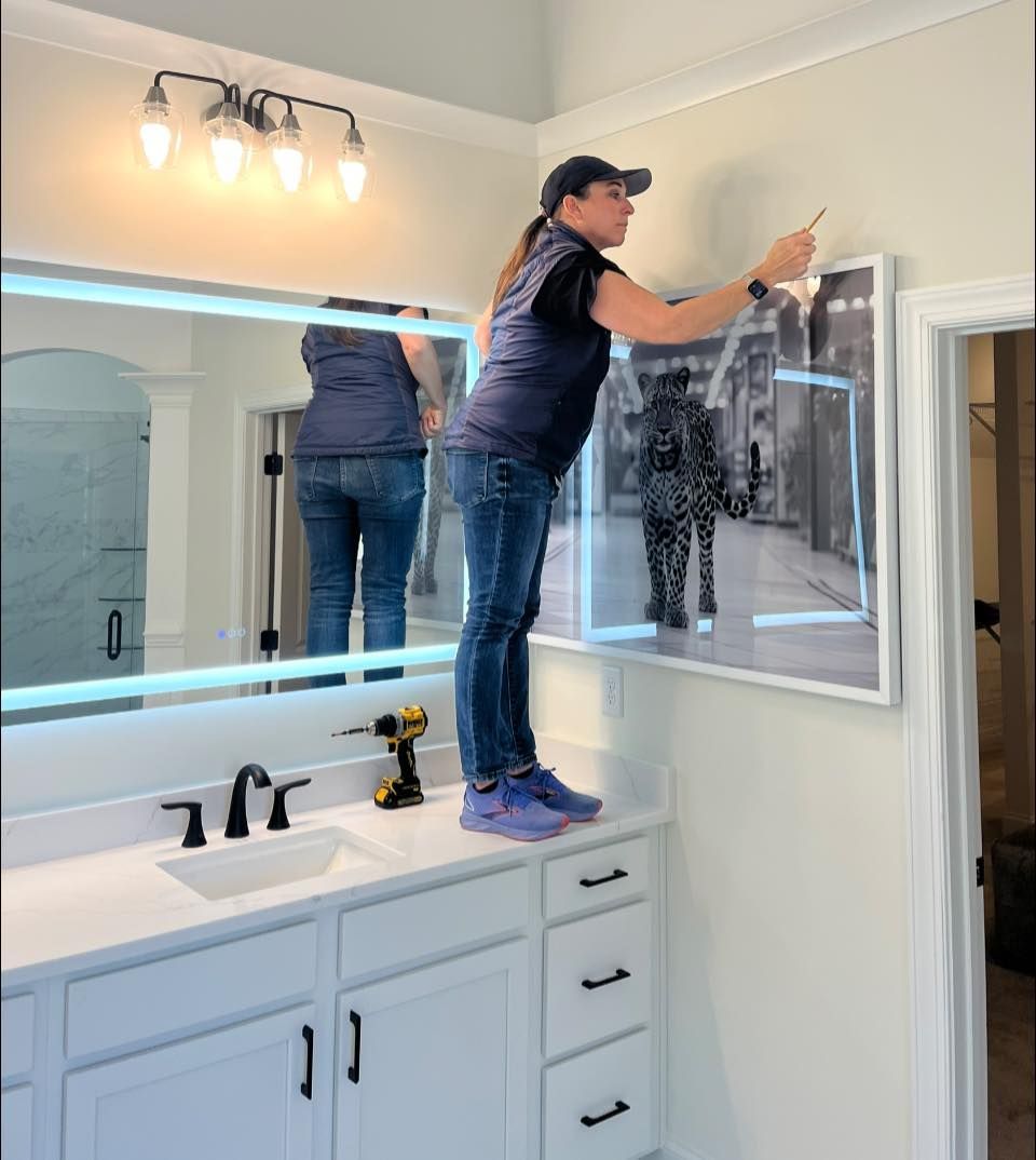 Person cleaning a bathroom mirror above a white vanity with a spray bottle and cloth