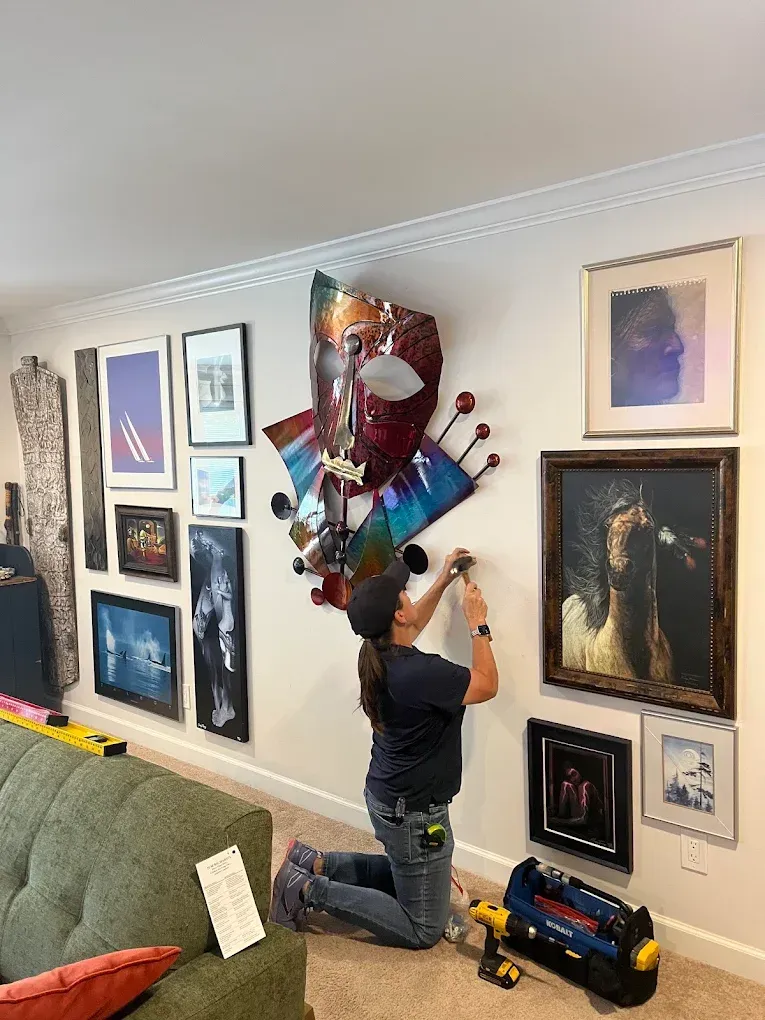 Person kneeling to hang a colorful wall sculpture in a living room gallery wall