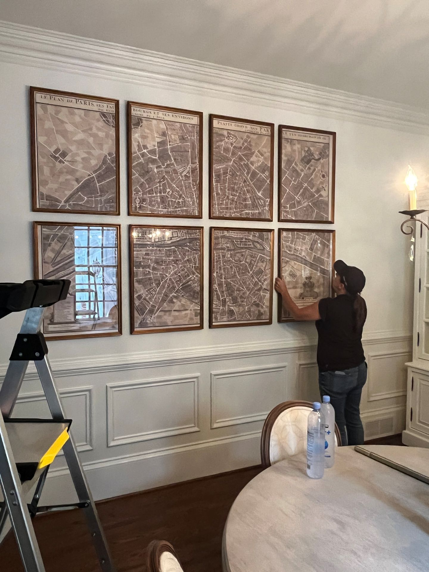 Two people hanging framed artwork in a white-paneled living room