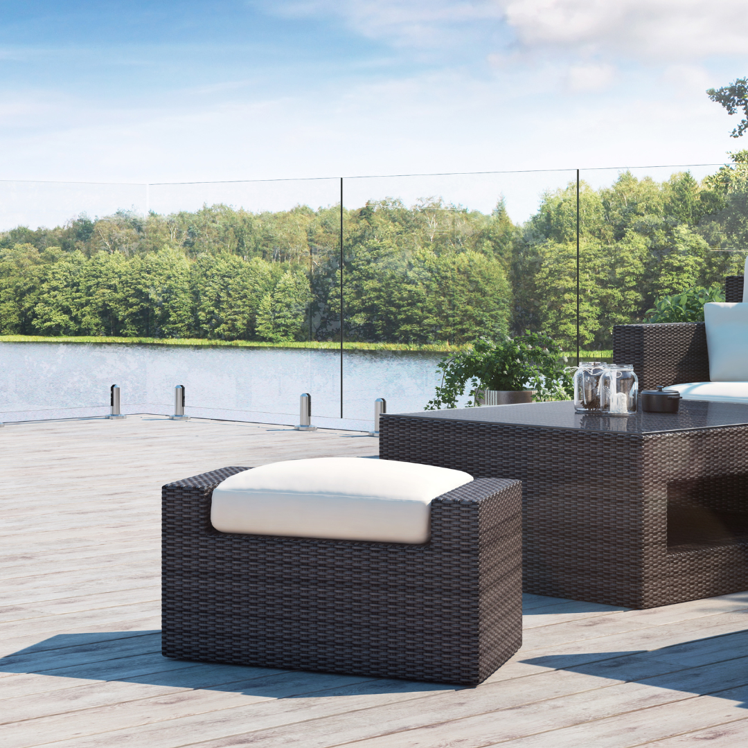 A patio with wicker furniture and a glass railing overlooking a lake