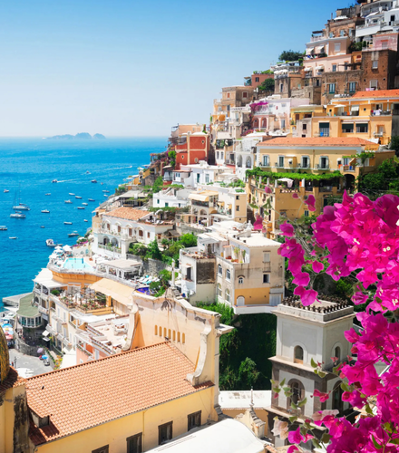 Colorful villas stacked on a cliffside overlooking the blue sea in Positano, Italy, with bright pink bougainvillea.