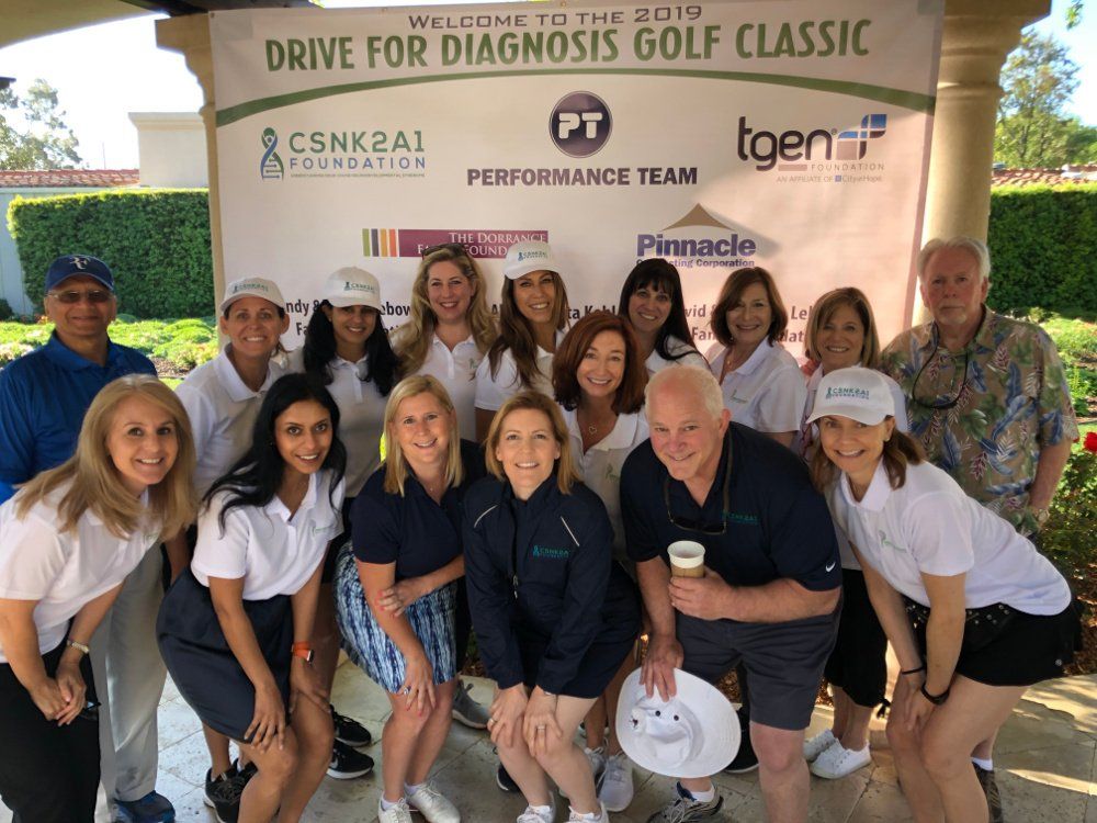 A group of people standing in front of a sign that says drive for diagnosis golf classic