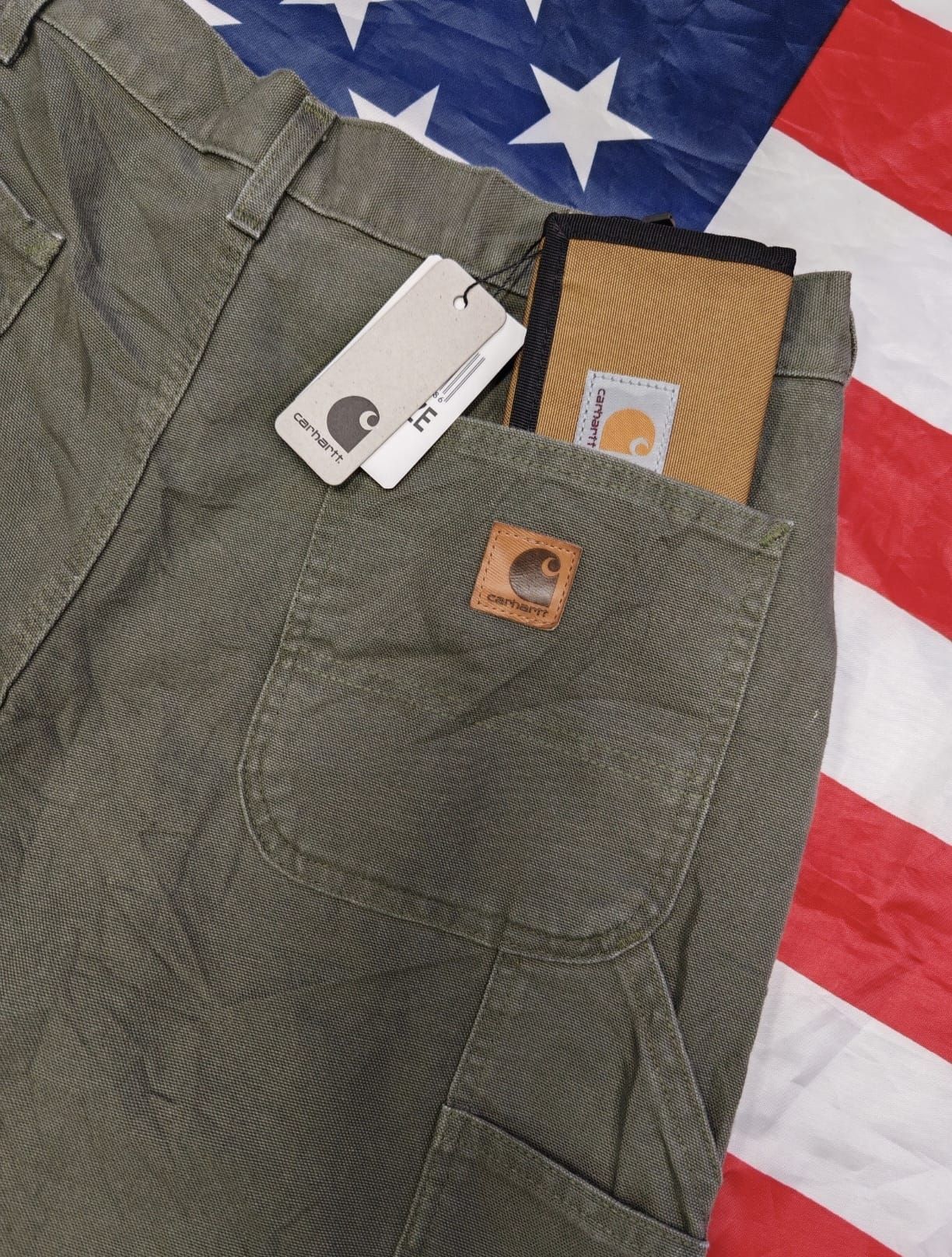 Taschino di giacca verde oliva con portafoglio color cuoio e carta bianca su sfondo con la bandiera americana.