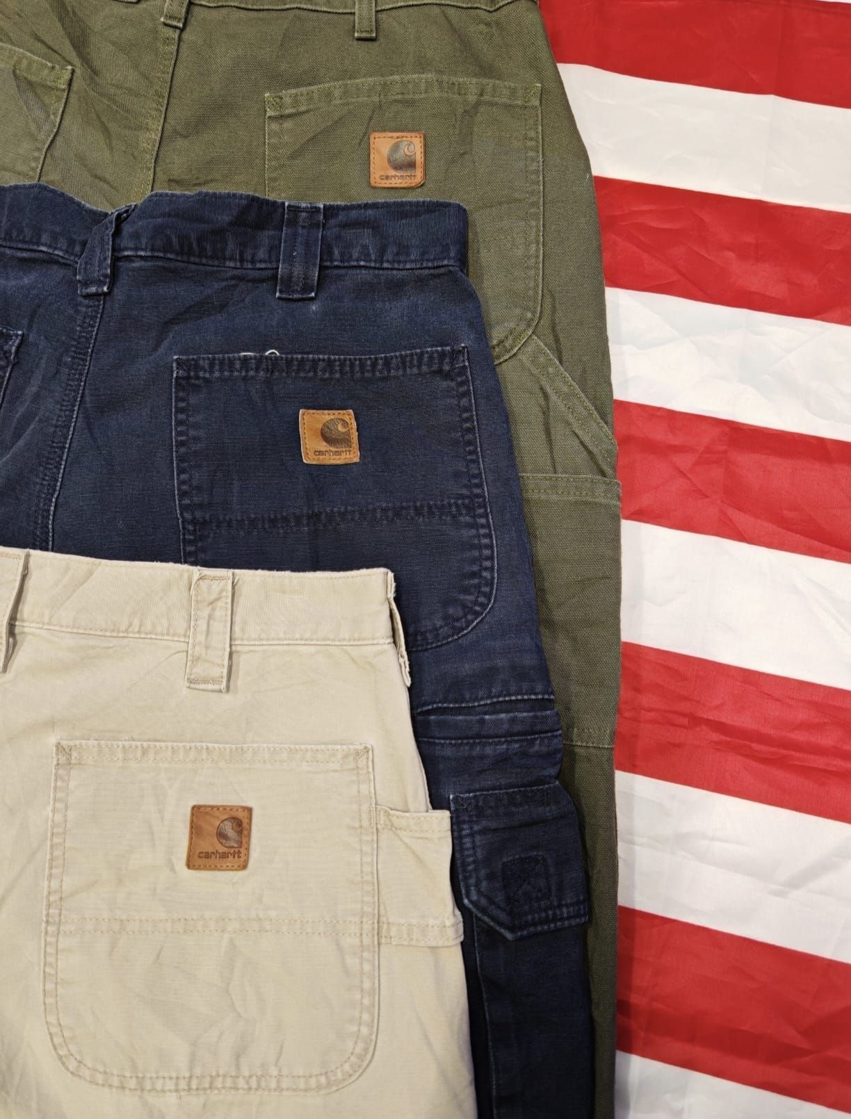 Pantaloni sovrapposti color kaki, blu navy e verde oliva su uno sfondo a righe rosse e bianche.
