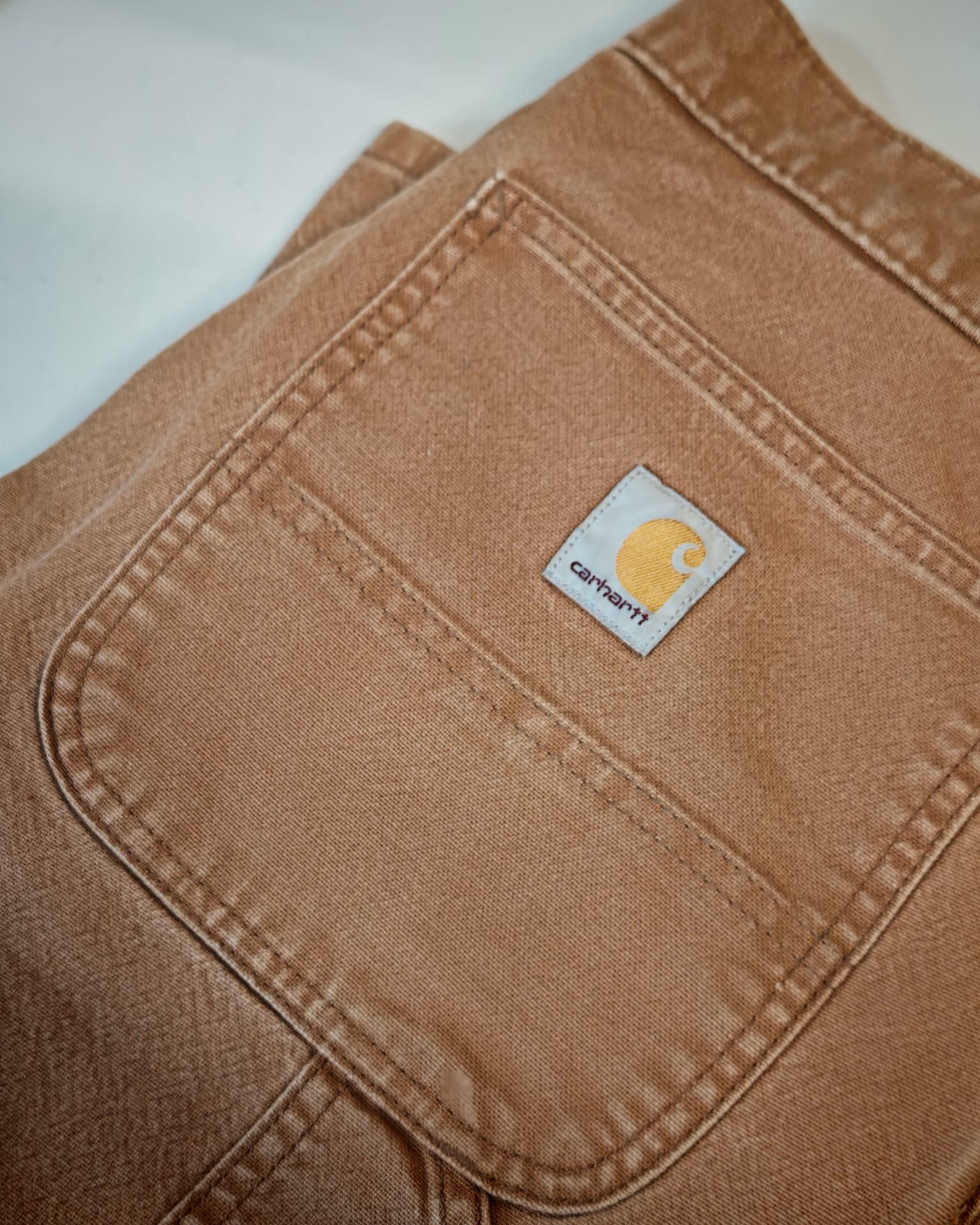 Primo piano di una tasca in denim color cachi con una piccola toppa con il logo Carhartt.
