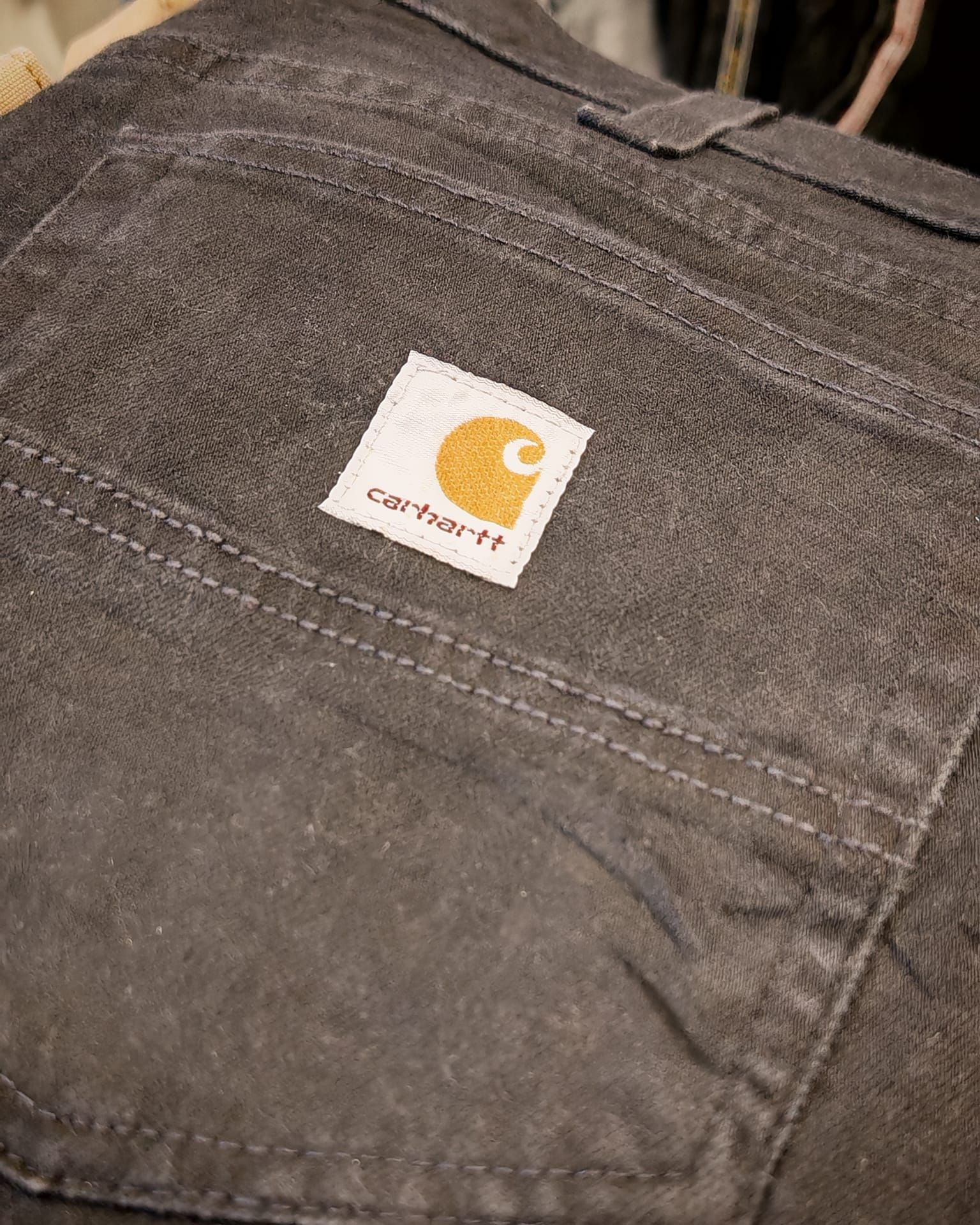 Primo piano di una tasca di un paio di jeans Carhartt marroni con una toppa con il logo bianco.