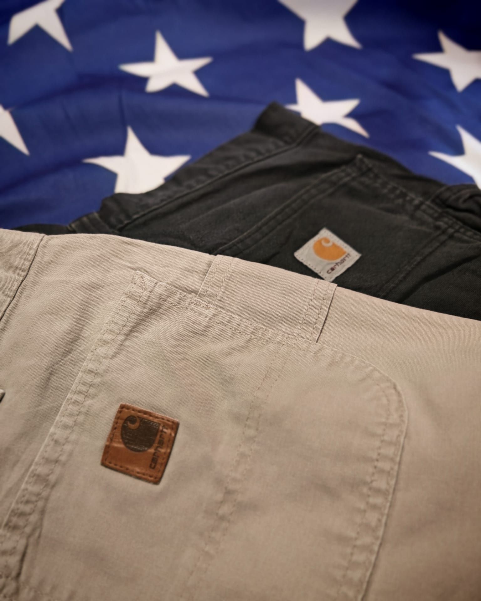 Tre paia di pantaloni su una coperta blu a stelle: pantaloncini di jeans neri, beige e marrone chiaro con logo.