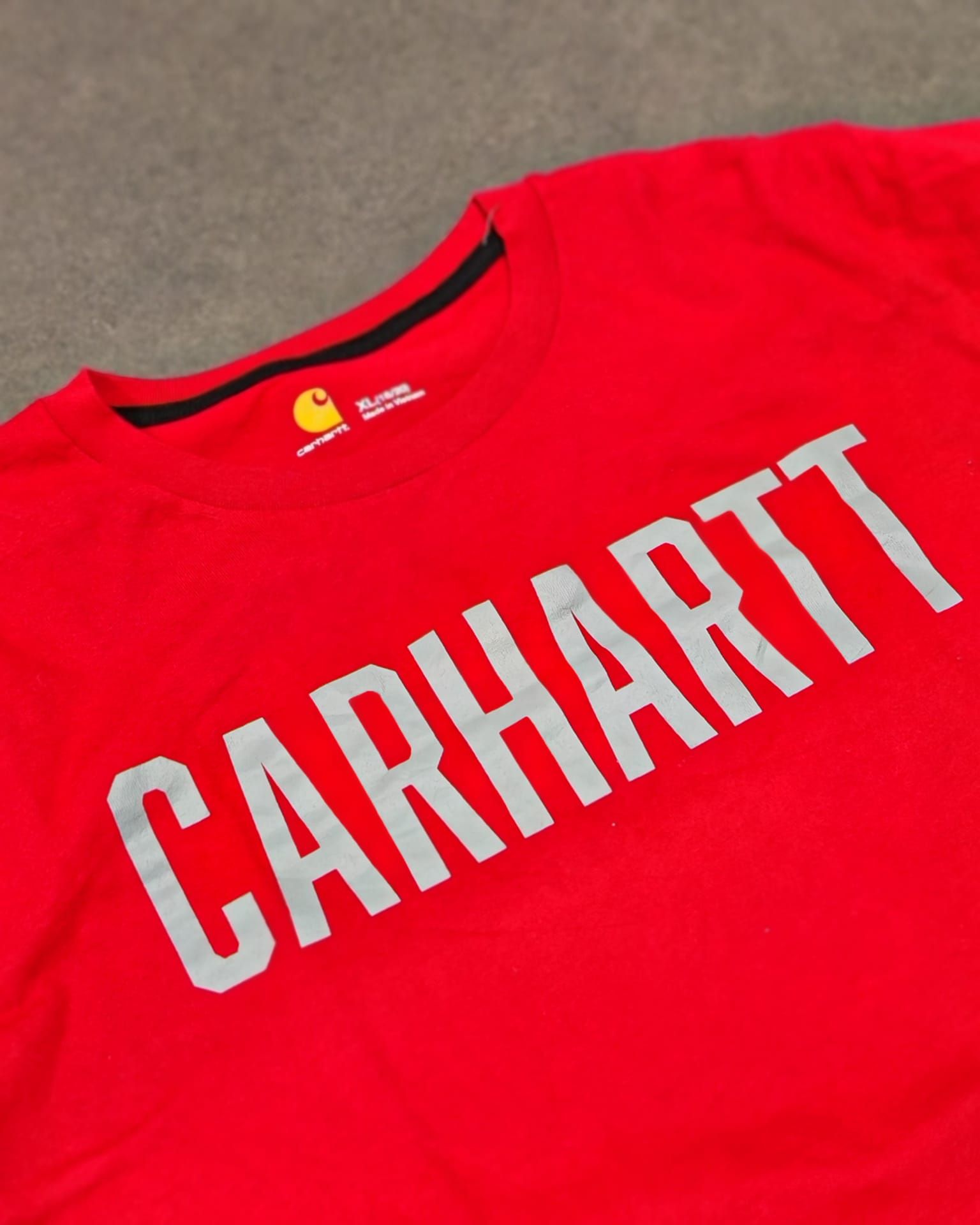 T-shirt rossa Carhartt con grandi scritte bianche su sfondo scuro.