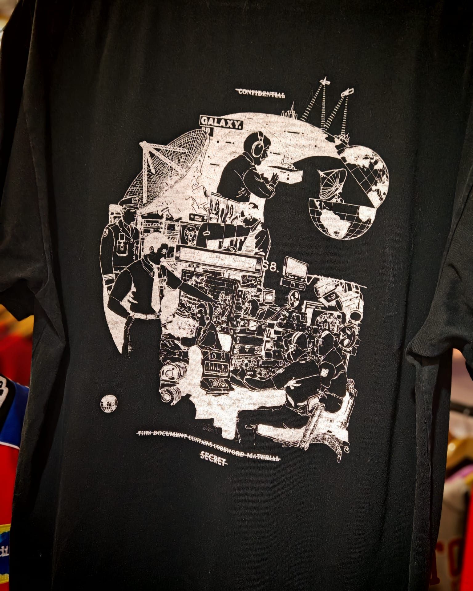T-shirt nera con una grafica astratta a collage bianca sul petto, esposta su una gruccia.