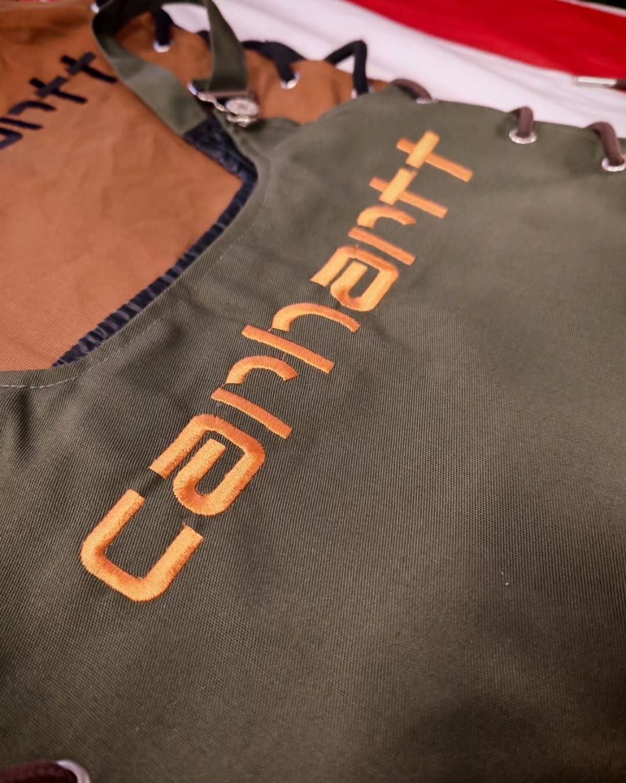 Primo piano di una borsa Carhartt color beige e verde oliva con logo arancione e finiture nere.