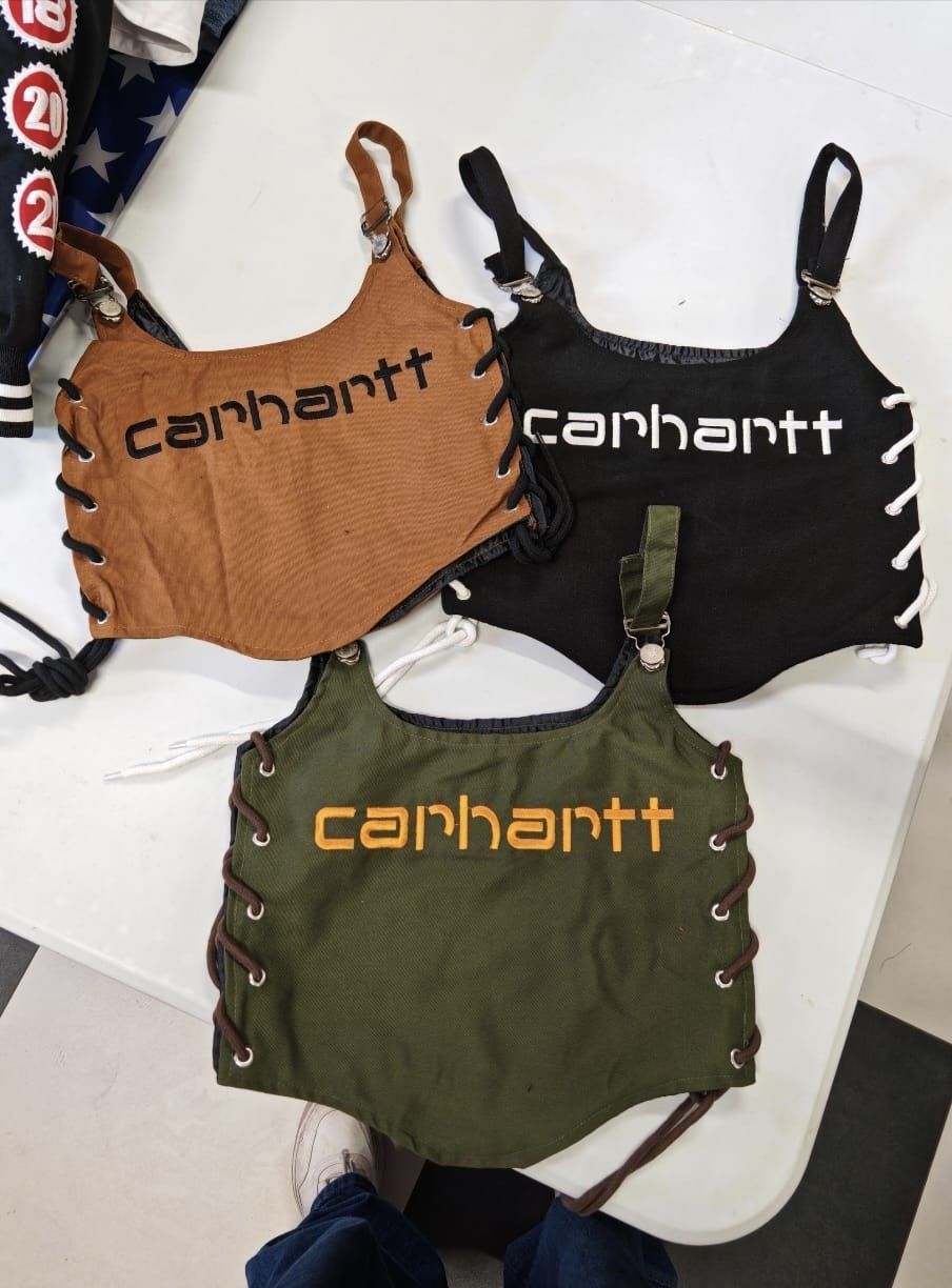 Tre top corti Carhartt color beige, nero e verde oliva disposti su una superficie bianca