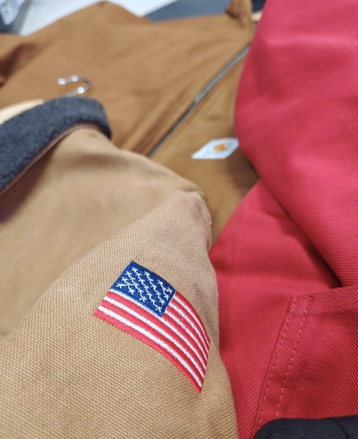 Primo piano della manica di una giacca color cachi con una piccola toppa raffigurante la bandiera americana, accanto a una borsa rossa.