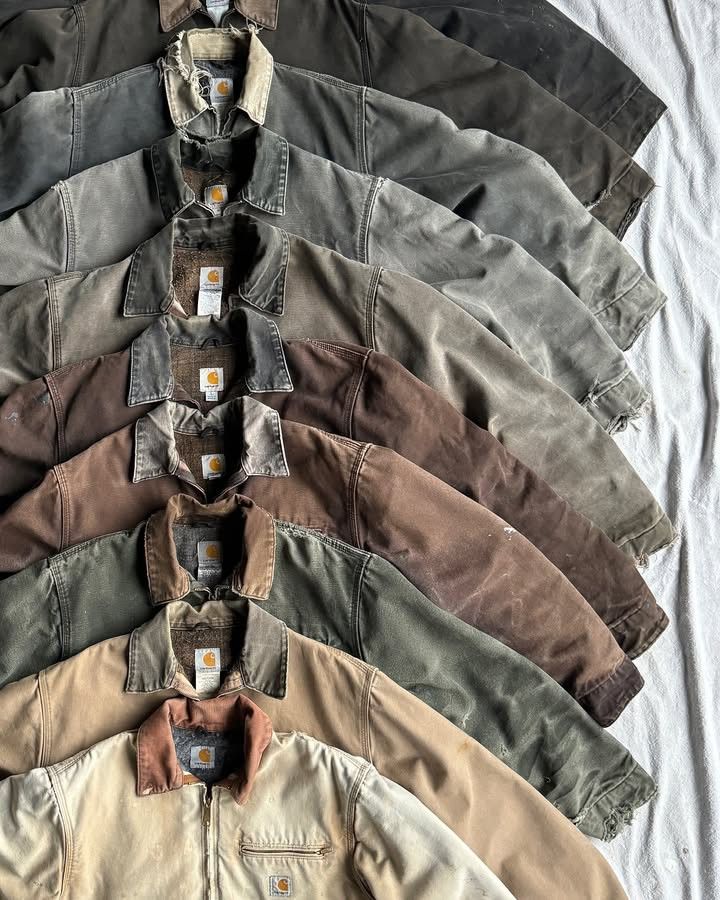 Una pila di giacche abbottonate di colore grigio, verde, marrone e beige, disposte su una superficie bianca.