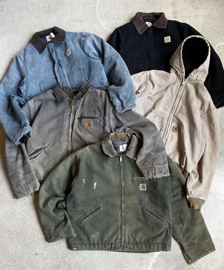 Quattro giacche da lavoro nei colori blu, grigio, nero e verde oliva sono disposte su una superficie beige.