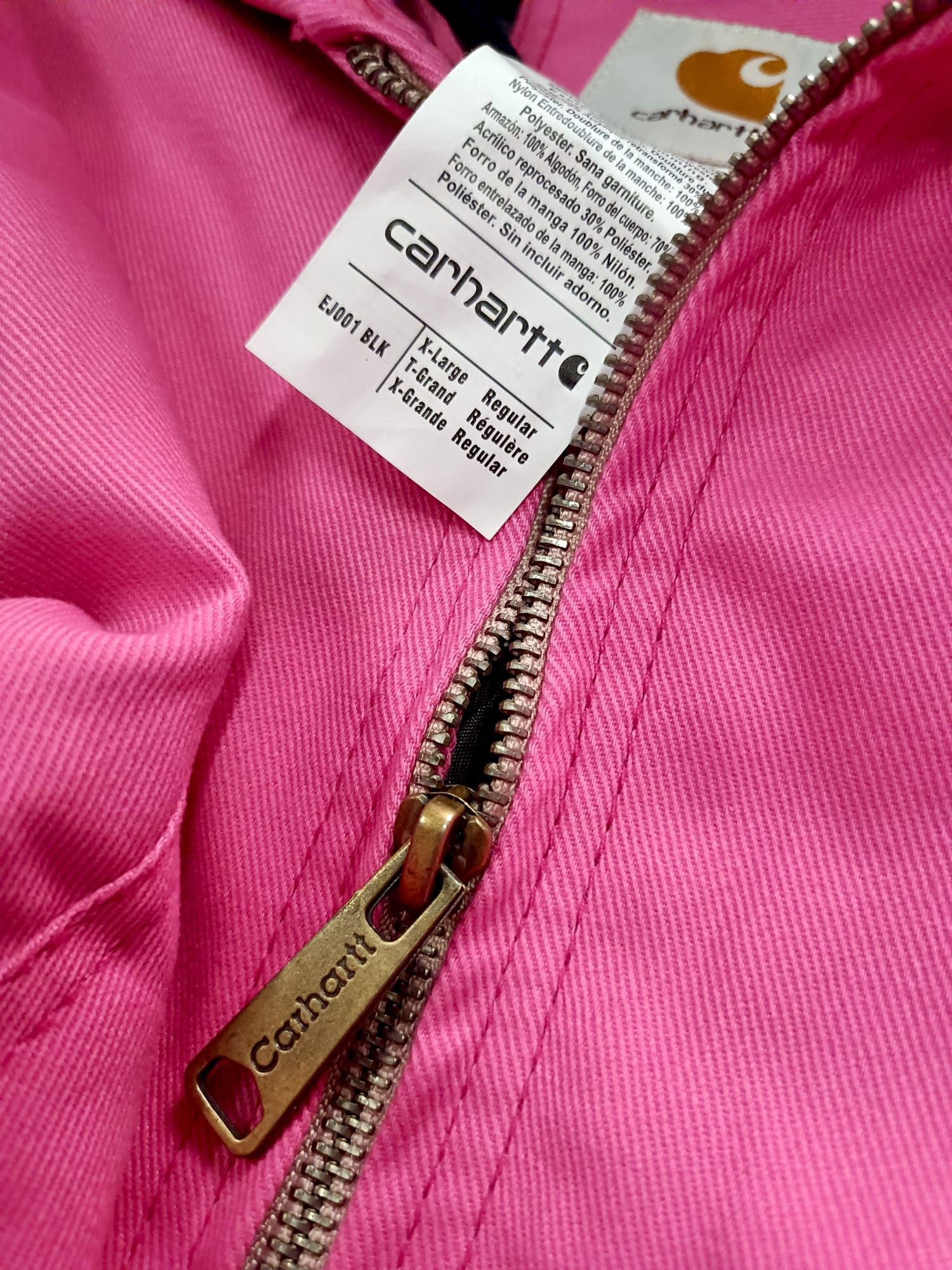 Primo piano della cerniera e delle etichette di una giacca Carhartt rosa.