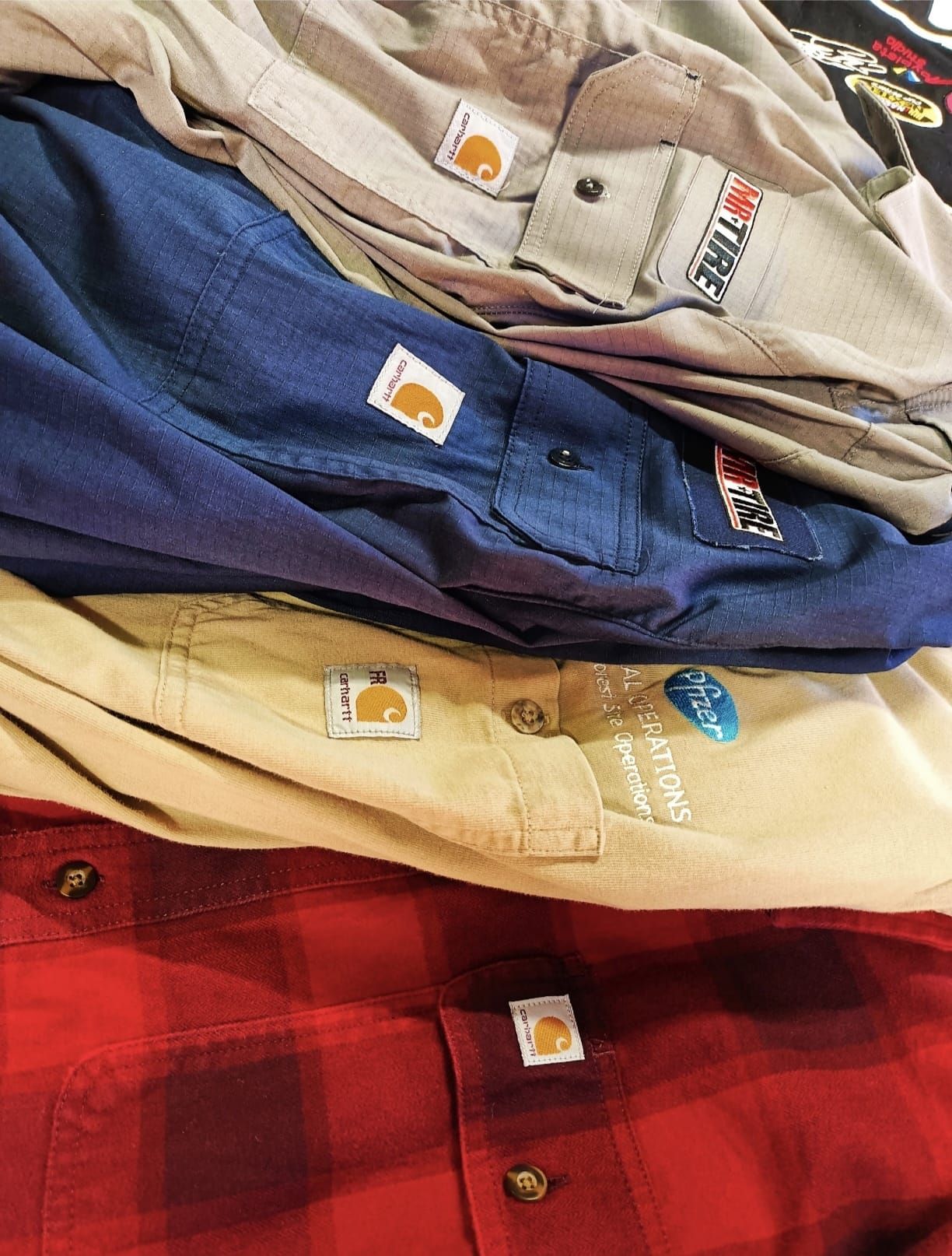 Pila di camicie piegate a quadri beige, blu scuro, marrone chiaro e rossi su uno scaffale di un negozio.
