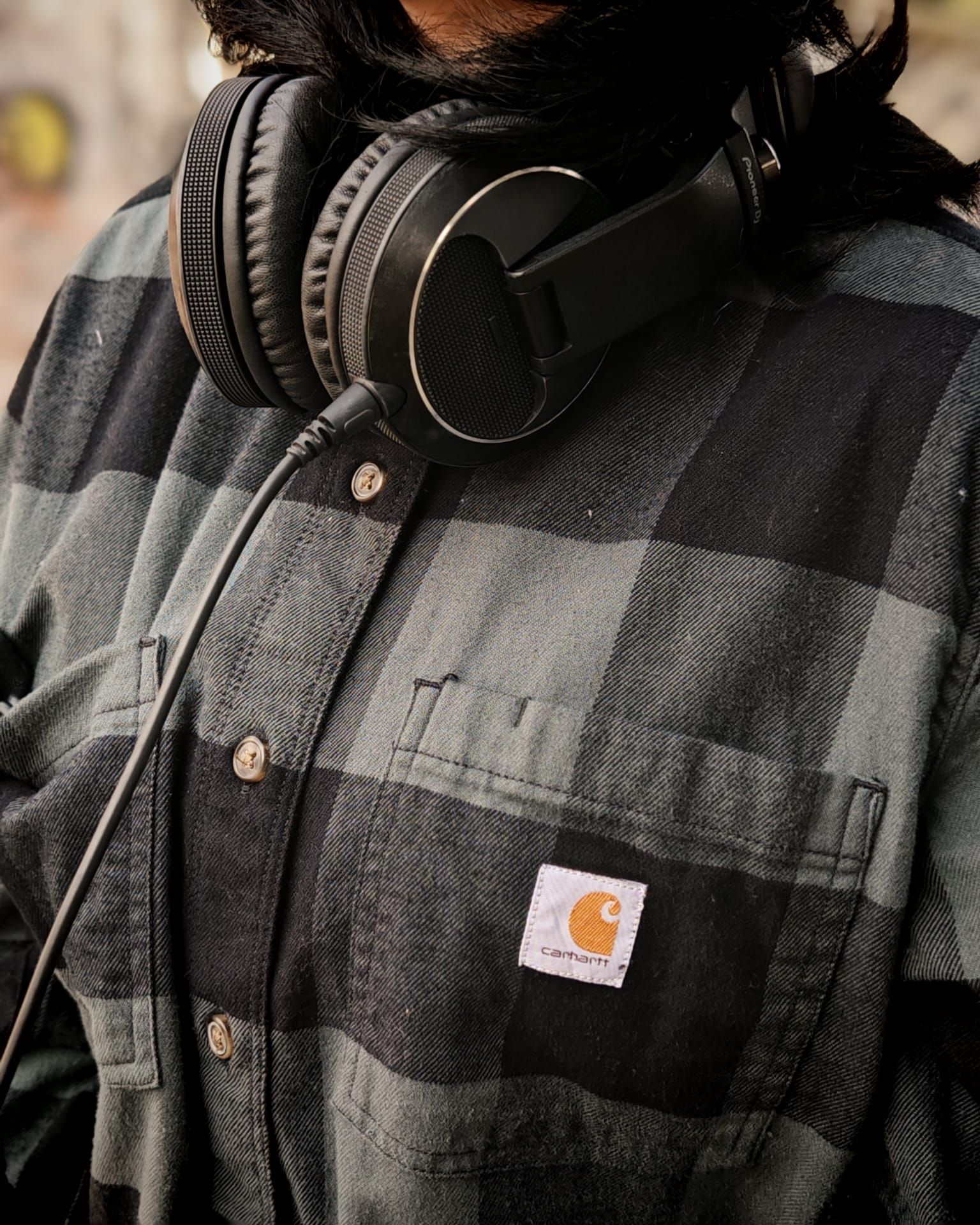Primo piano di una persona che indossa cuffie nere e una camicia a quadri grigia con una toppa con il logo Carhartt.