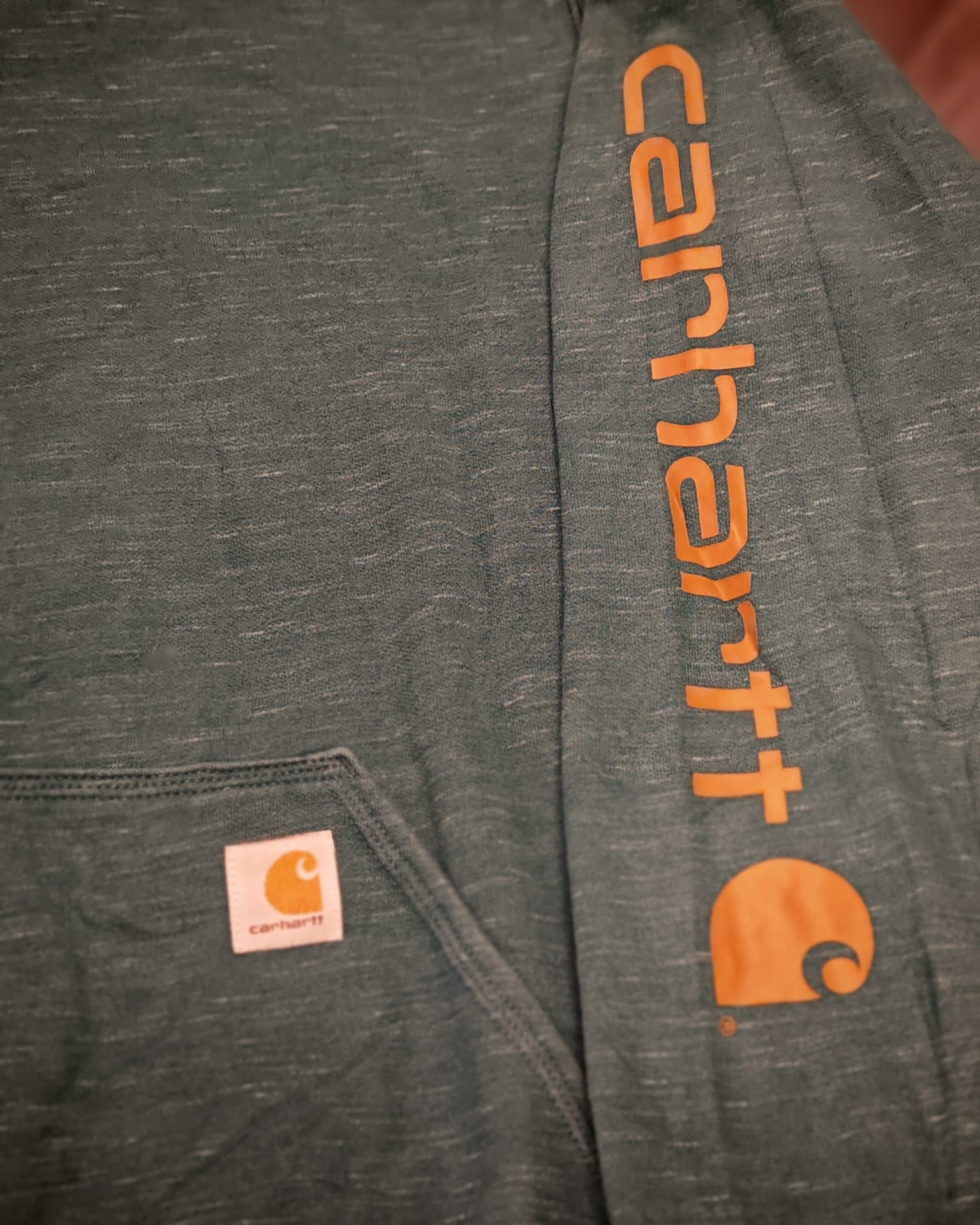 Camicia grigia Carhartt con logo arancione e piccolo logo sulla tasca sul petto.