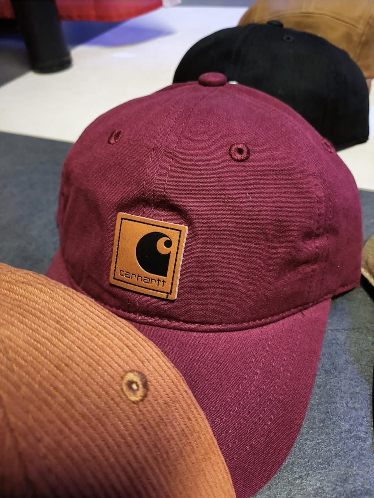 Tre cappellini da baseball impilati uno sull'altro, di cui uno bordeaux e uno nero, su un tavolo.