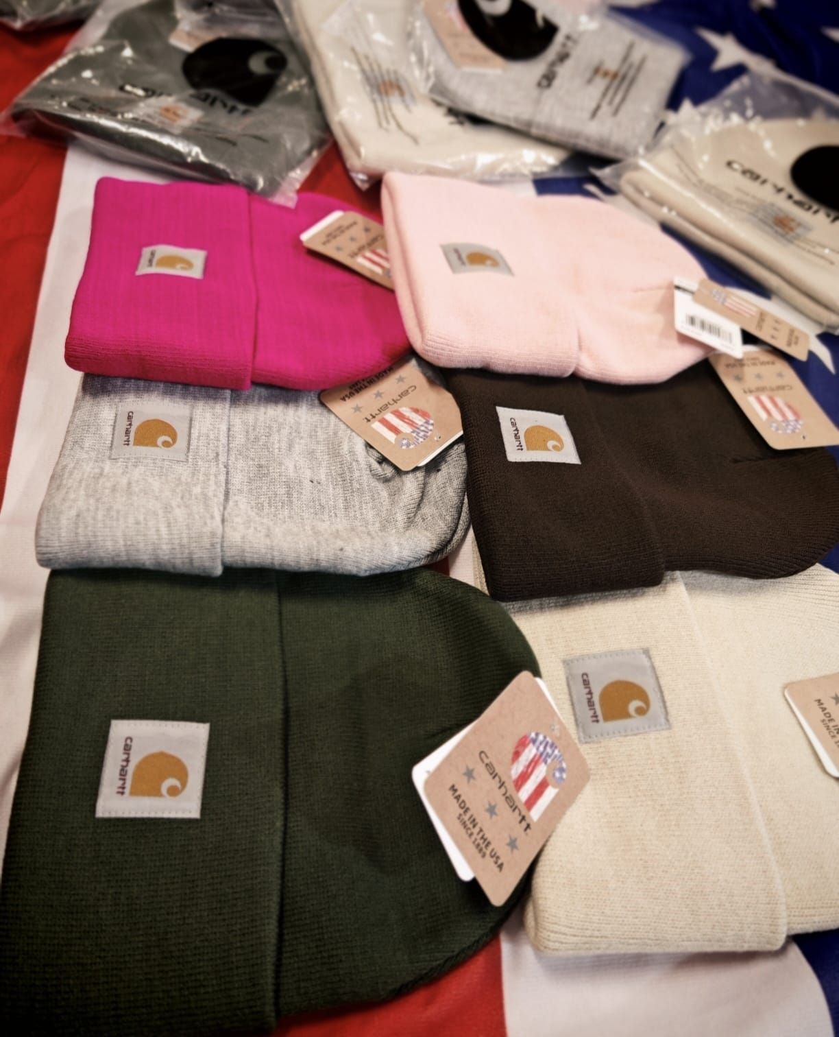 Maglioni piegati e impilati, nei colori rosa, bianco, nero, verde e crema, con piccole etichette con logo.