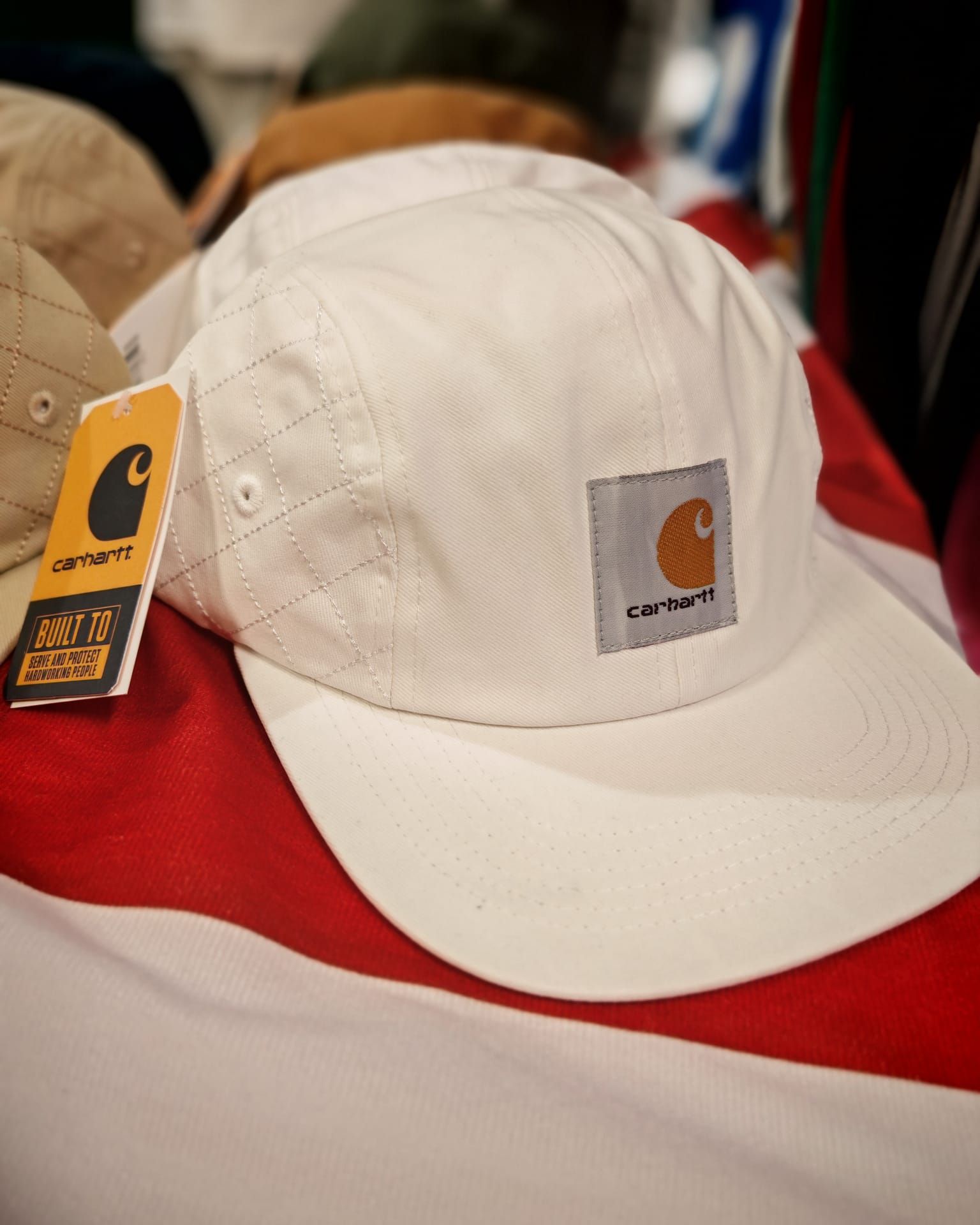 Cappellino bianco Carhartt con etichetta logo su sfondo rosso e bianco
