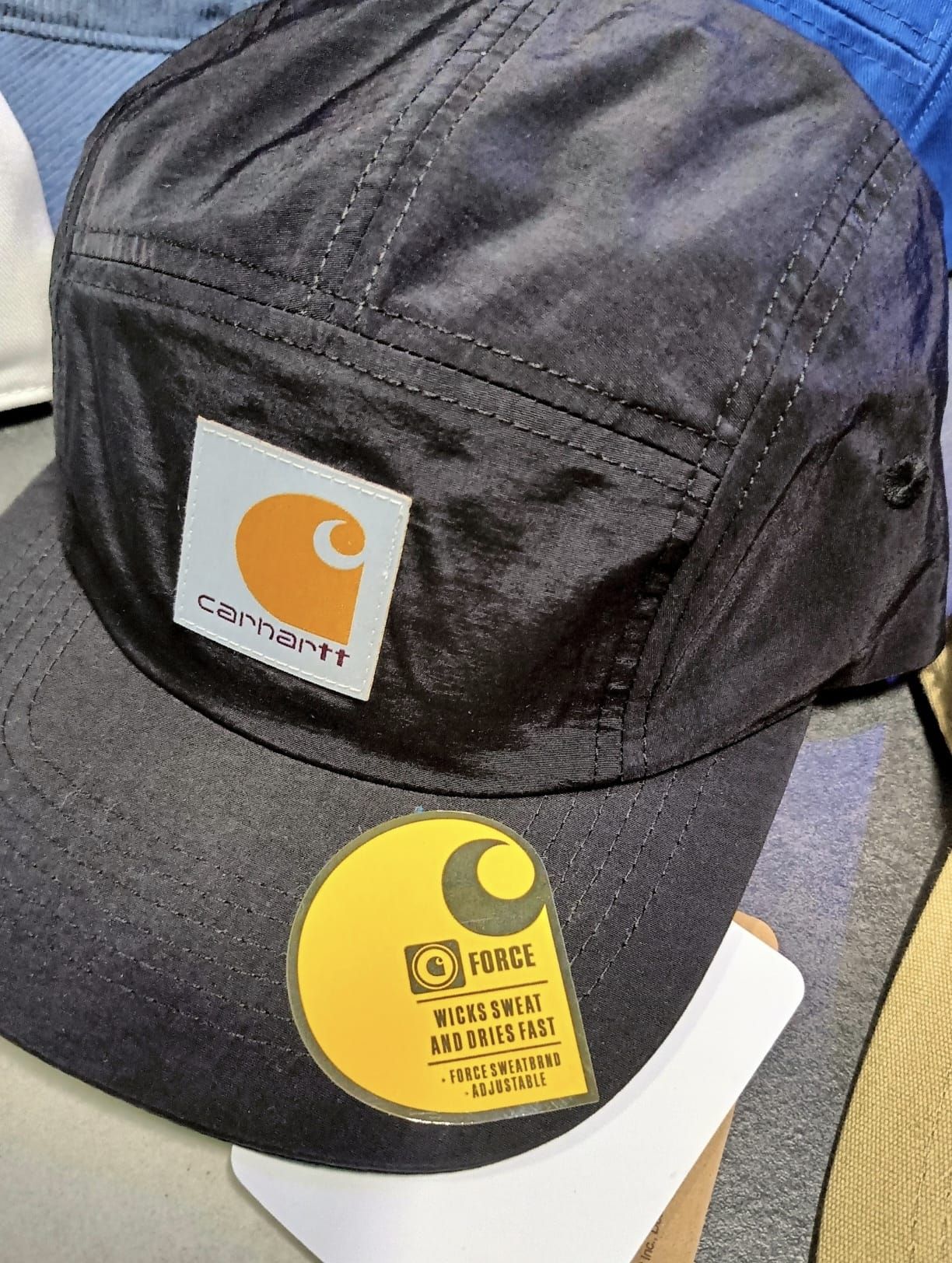 Cappellino nero Carhartt con patch logo arancioni e gialle sul davanti.