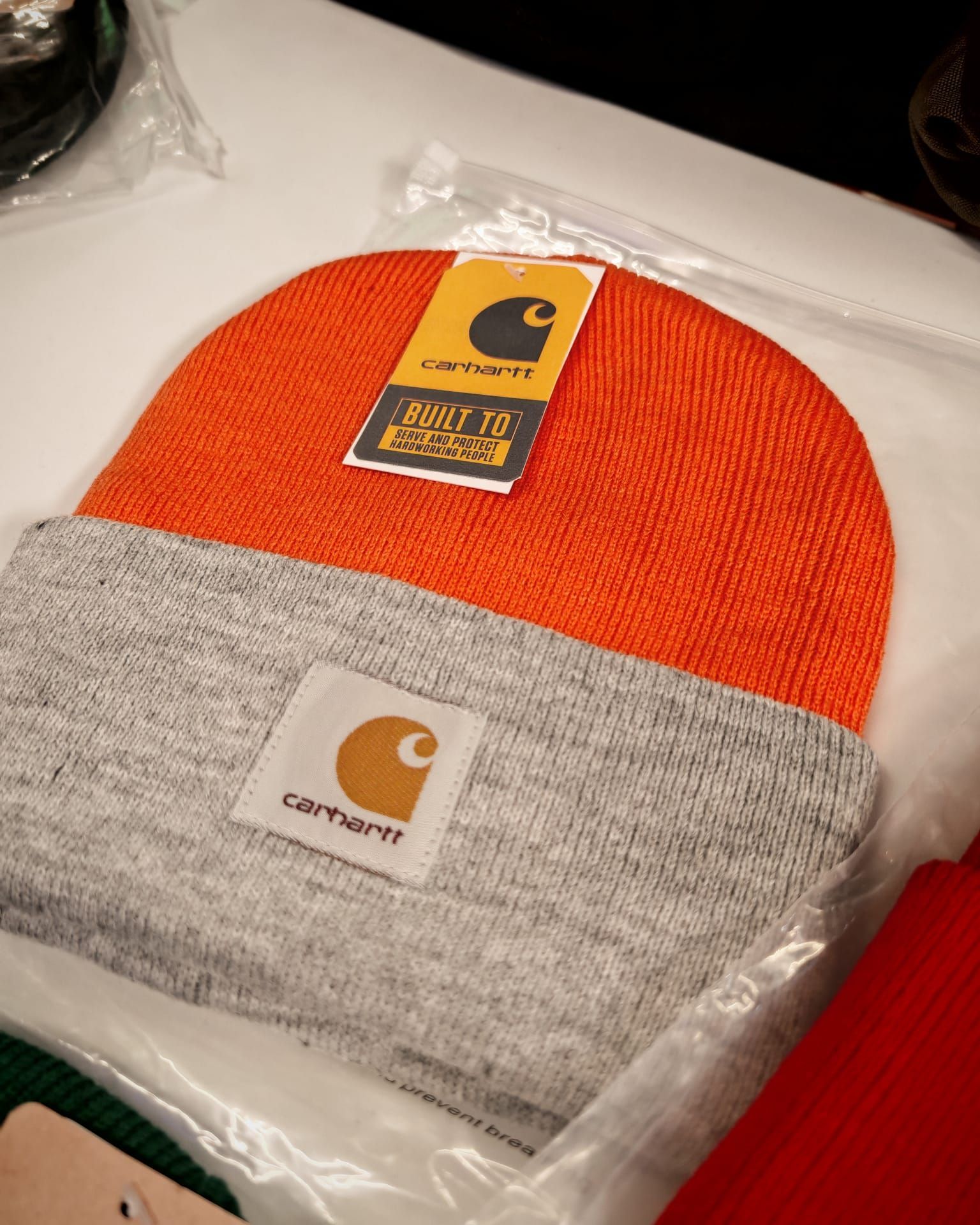 Berretto Carhartt arancione e grigio in confezione di plastica esposto in negozio.