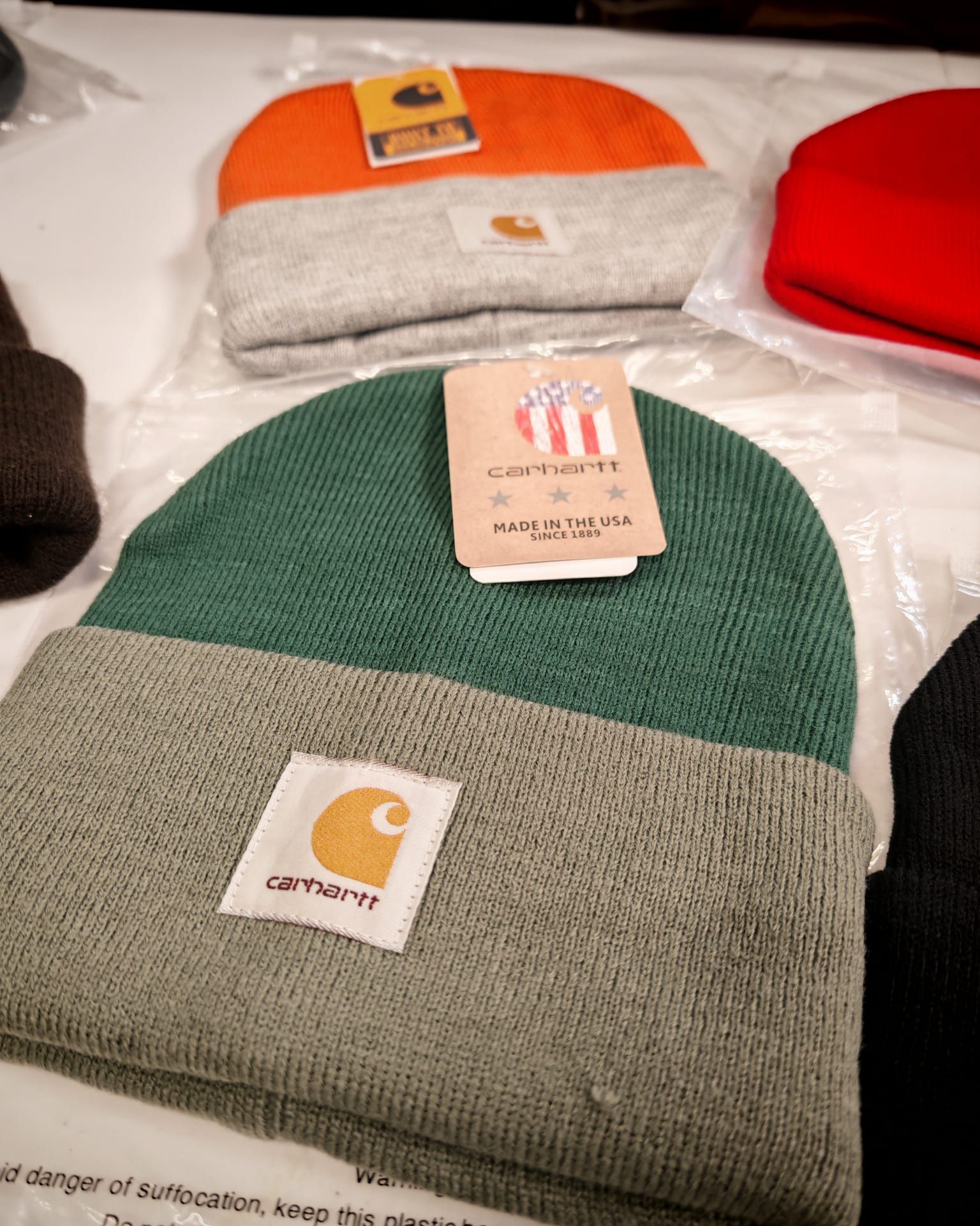 Berretti piegati di colore verde, arancione e rosso su un tavolo, con le etichette Carhartt ben visibili.
