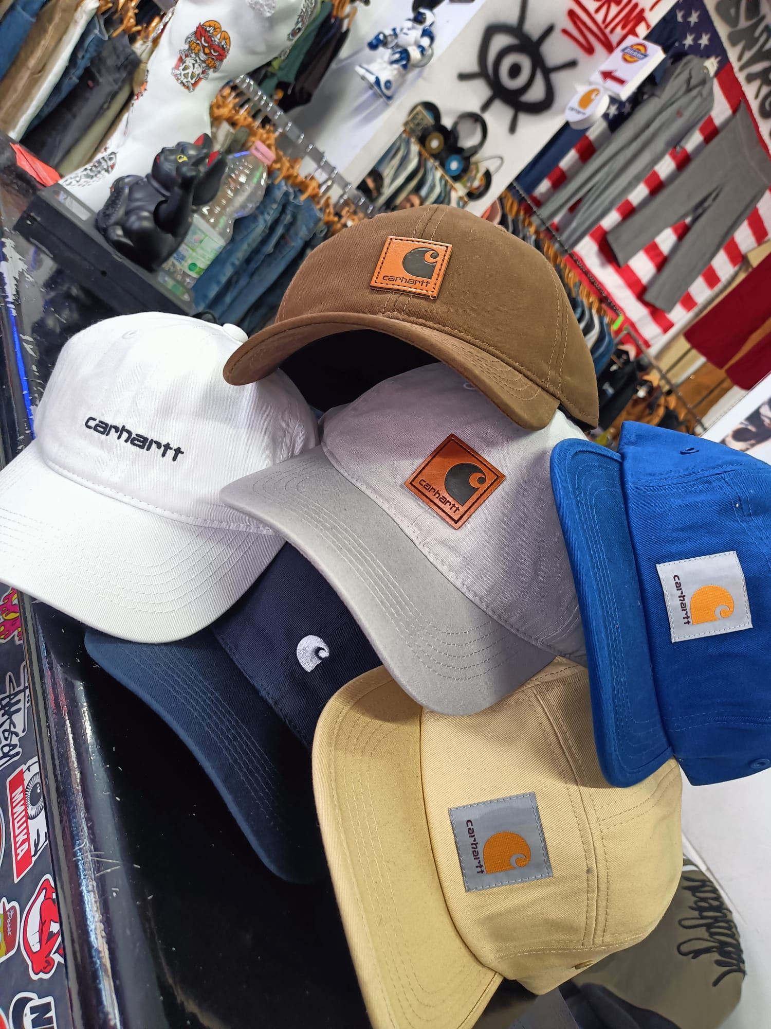 Cappellini da baseball Carhartt impilati su un espositore nei colori bianco, blu navy, beige e blu.