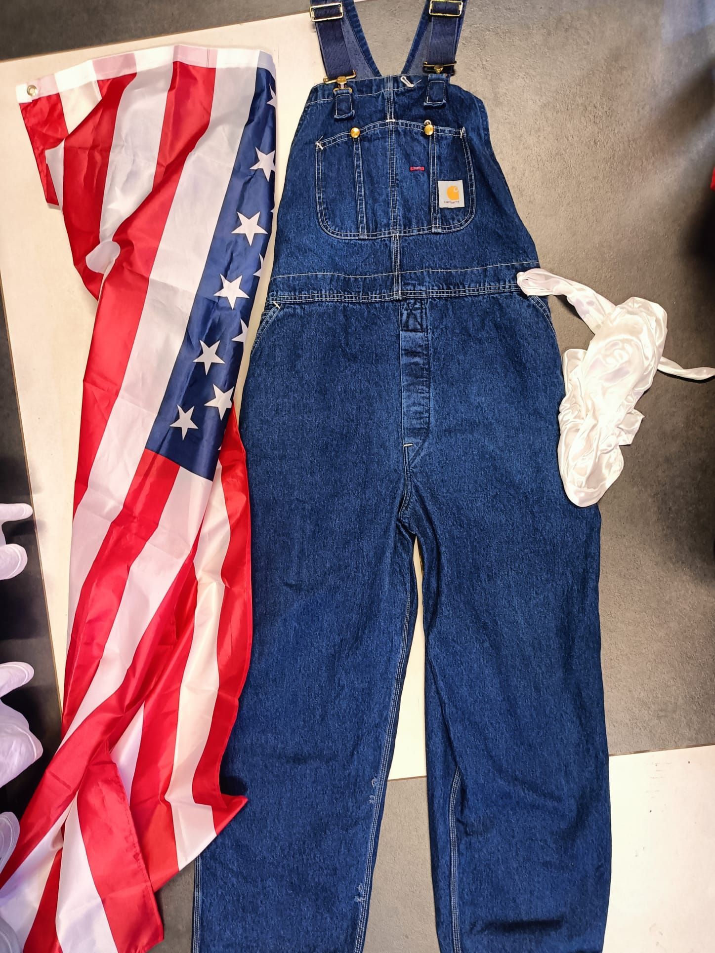 Una tuta di jeans blu accanto a una bandiera americana drappeggiata sul pavimento.
