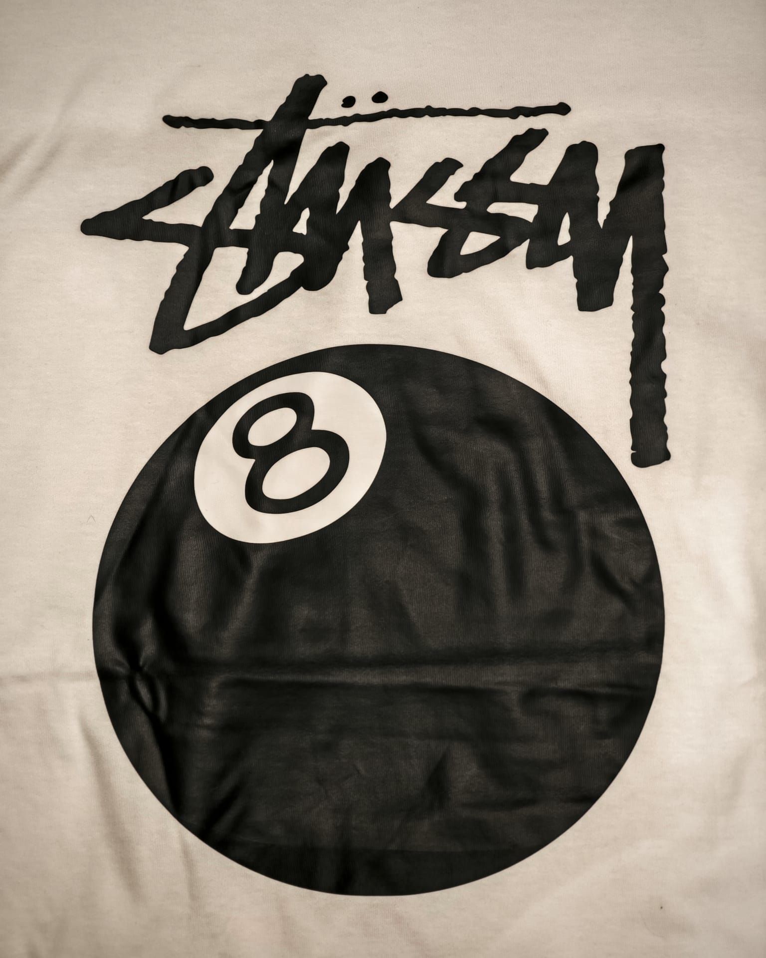 Maglietta nera Stüssy con una grande stampa nera raffigurante una palla numero 8 e logo bianco nella parte superiore.