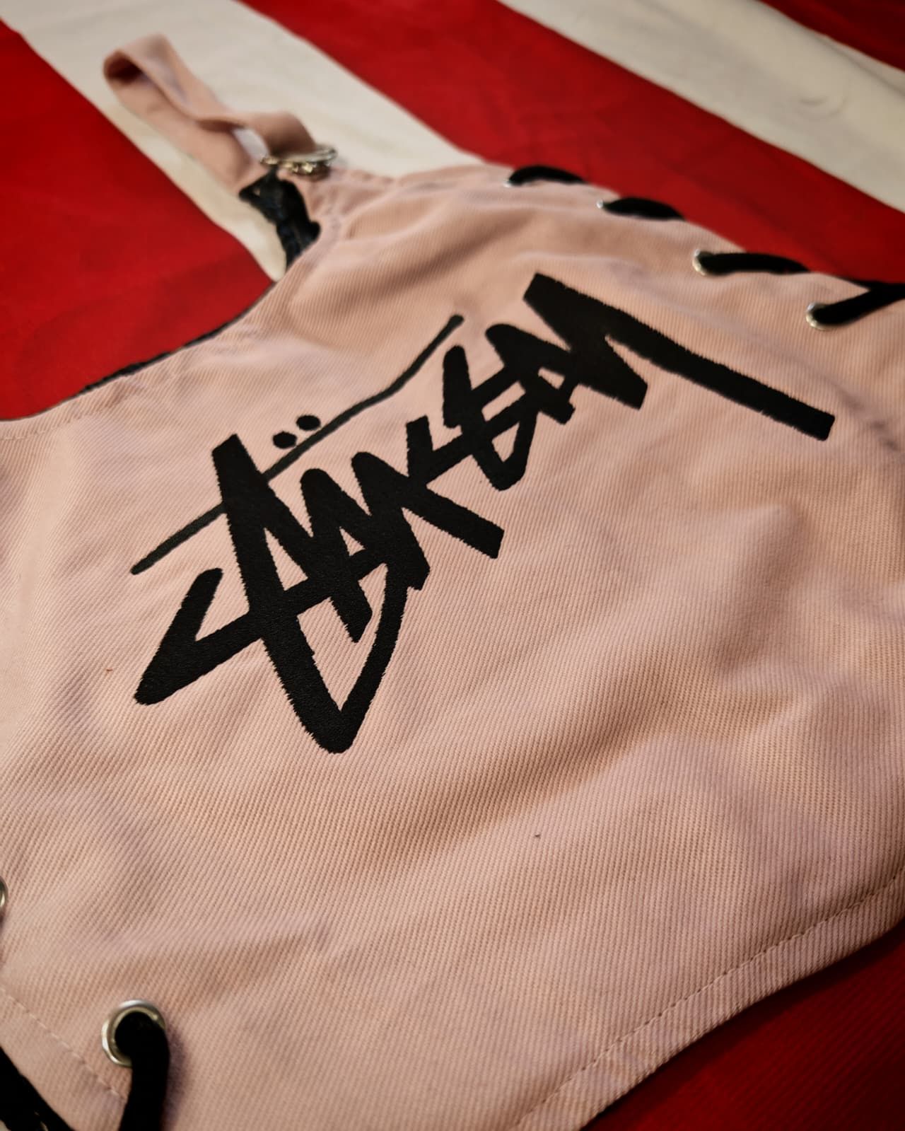 Borsa tote Stüssy beige con logo nero su sfondo a righe rosse e bianche.