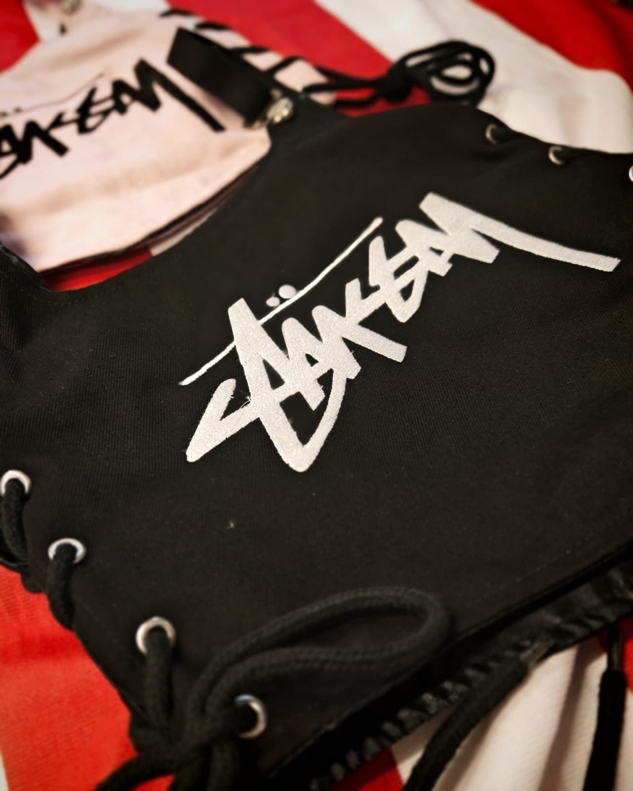 Sacchetti neri con coulisse e logo Stüssy bianco su sfondo rosso e bianco.