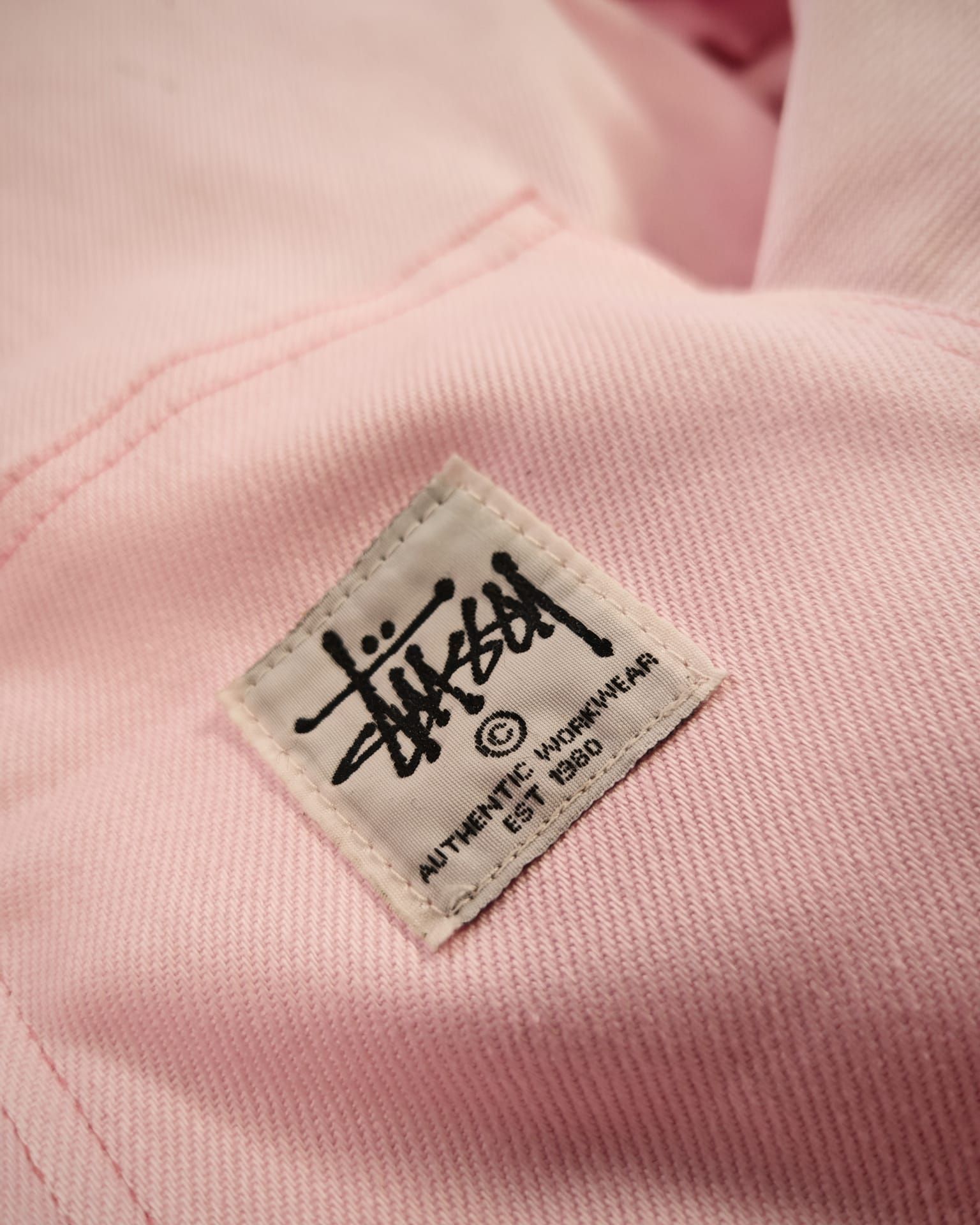 Primo piano di un'etichetta rosa di Stüssy cucita su un tessuto.