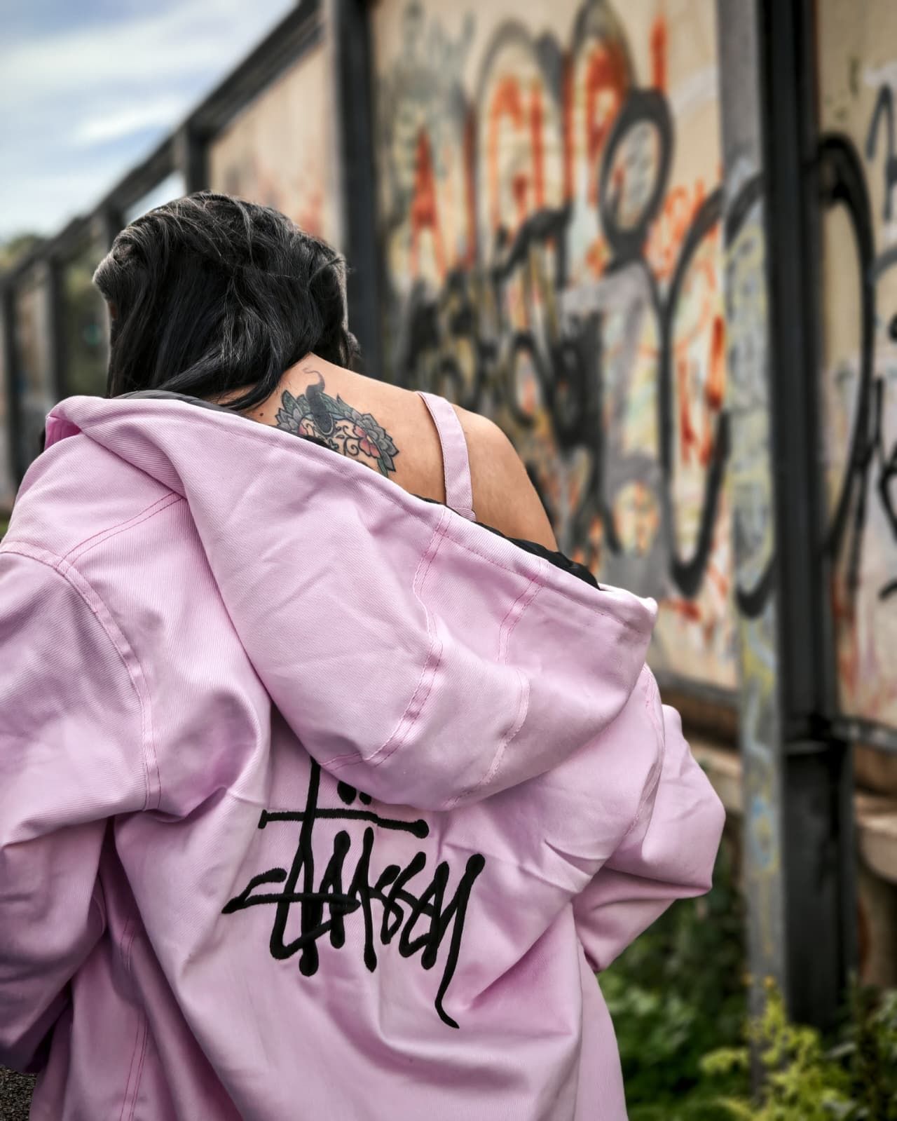 Una persona con una giacca rosa cammina accanto a muri ricoperti di graffiti in un vicolo cittadino.