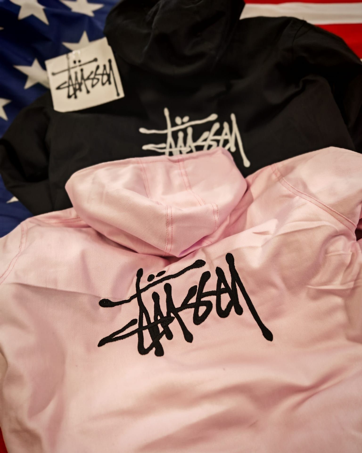 Felpe con cappuccio Stüssy rosa e nere sovrapposte, con logo del marchio sul petto e sull'etichetta.