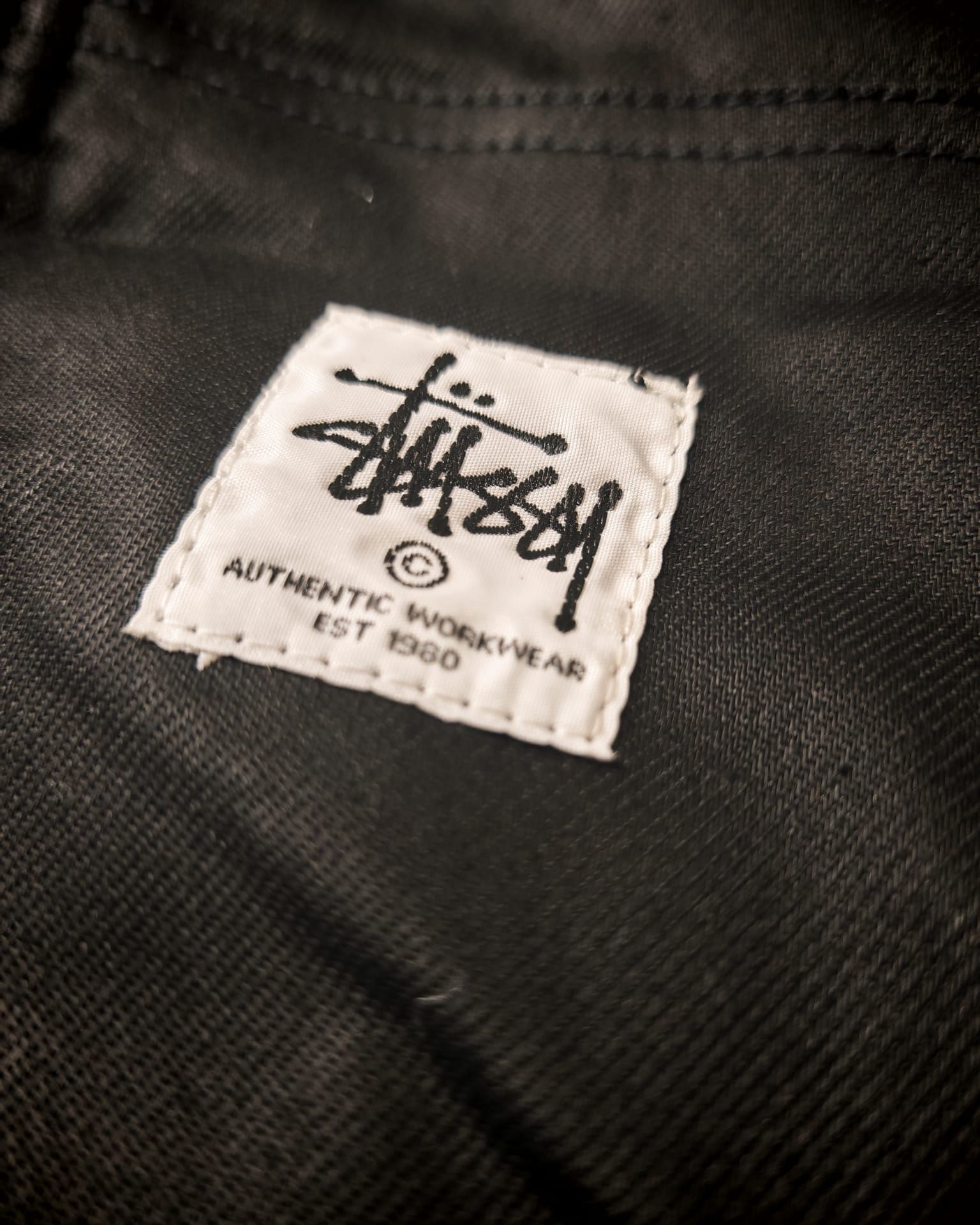 Primo piano di un'etichetta nera di Stüssy cucita all'interno di un capo d'abbigliamento.