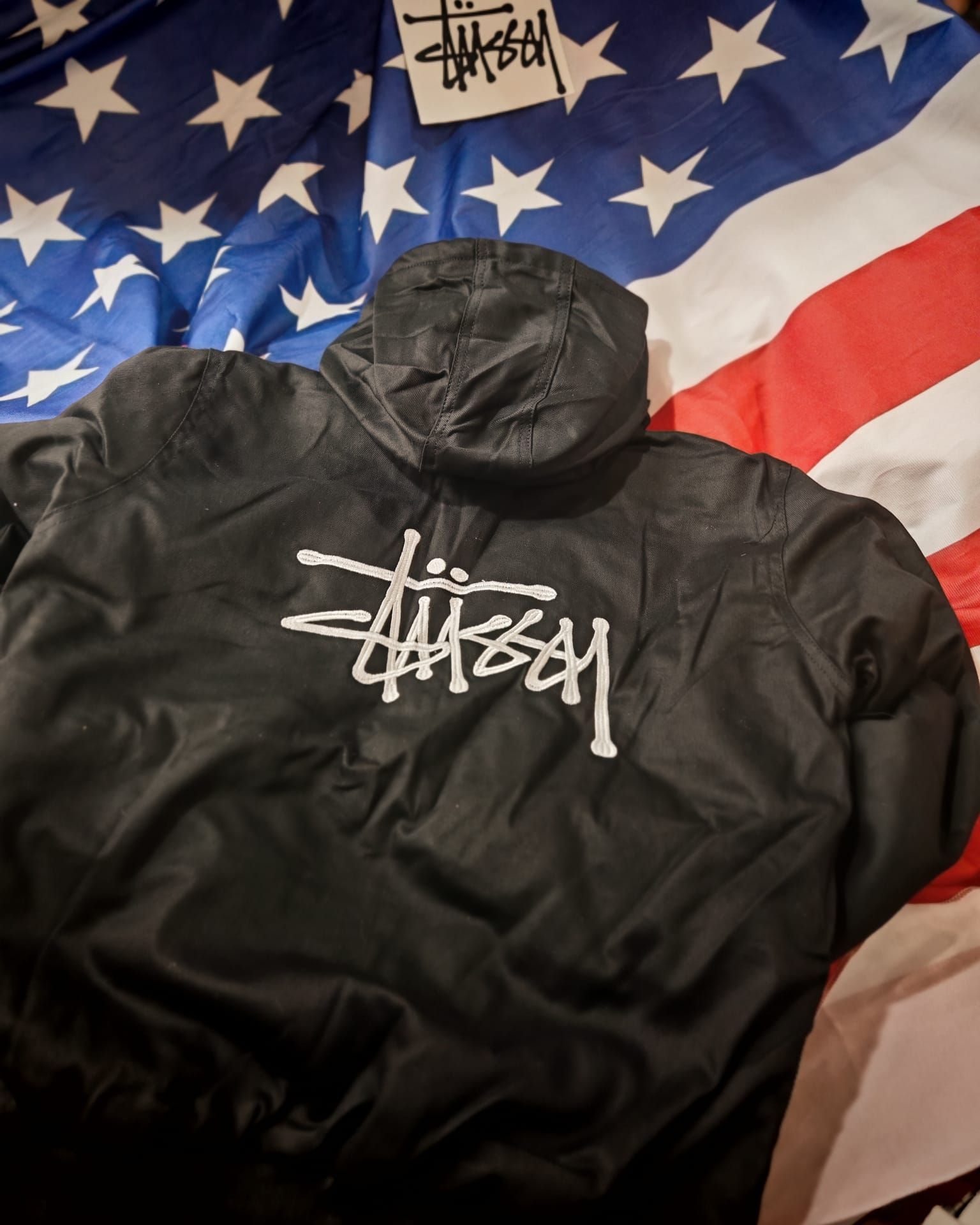 Giacca nera Stüssy adagiata su una coperta con la bandiera americana.