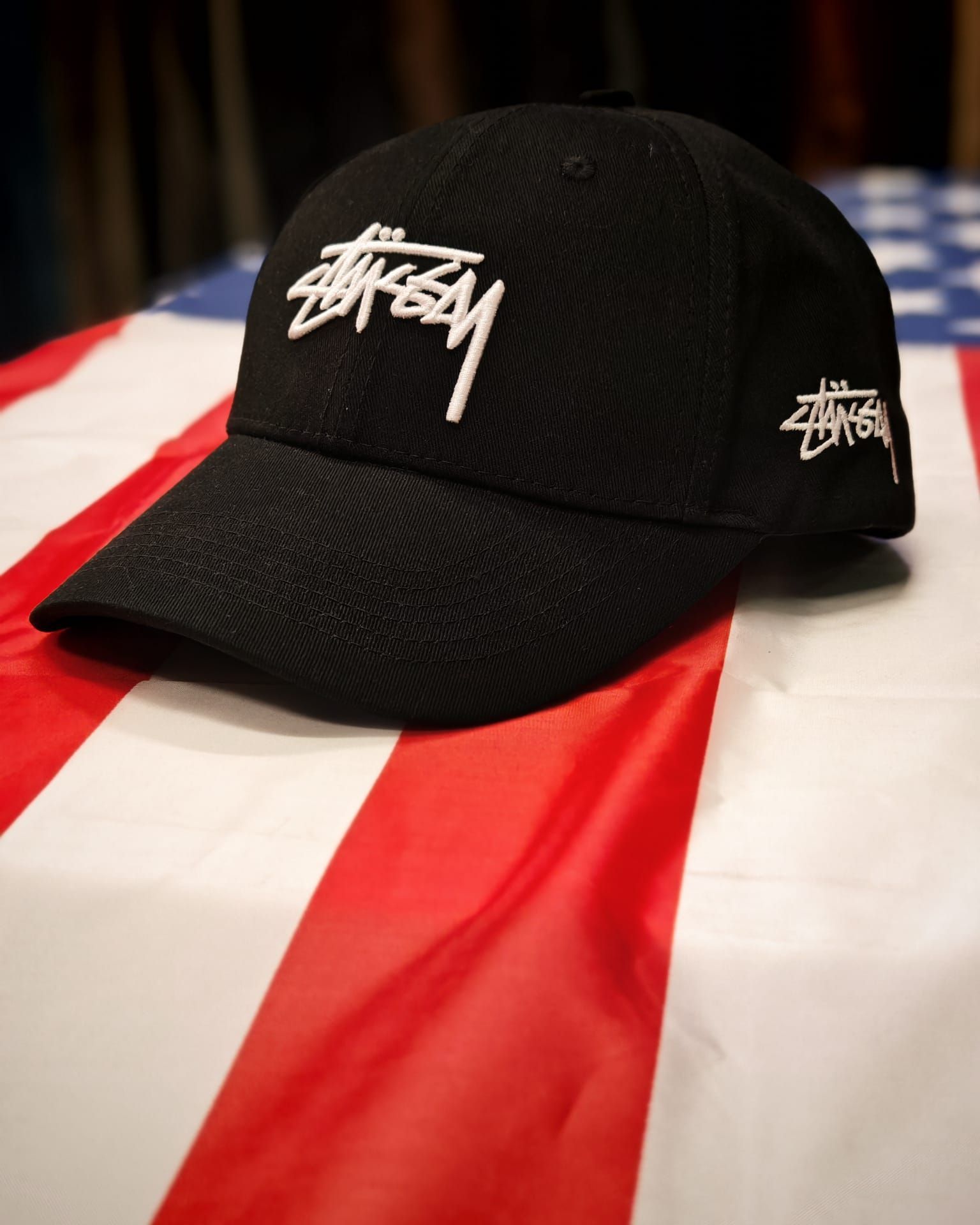 Berretto Stüssy nero su un panno a righe rosse, bianche e blu