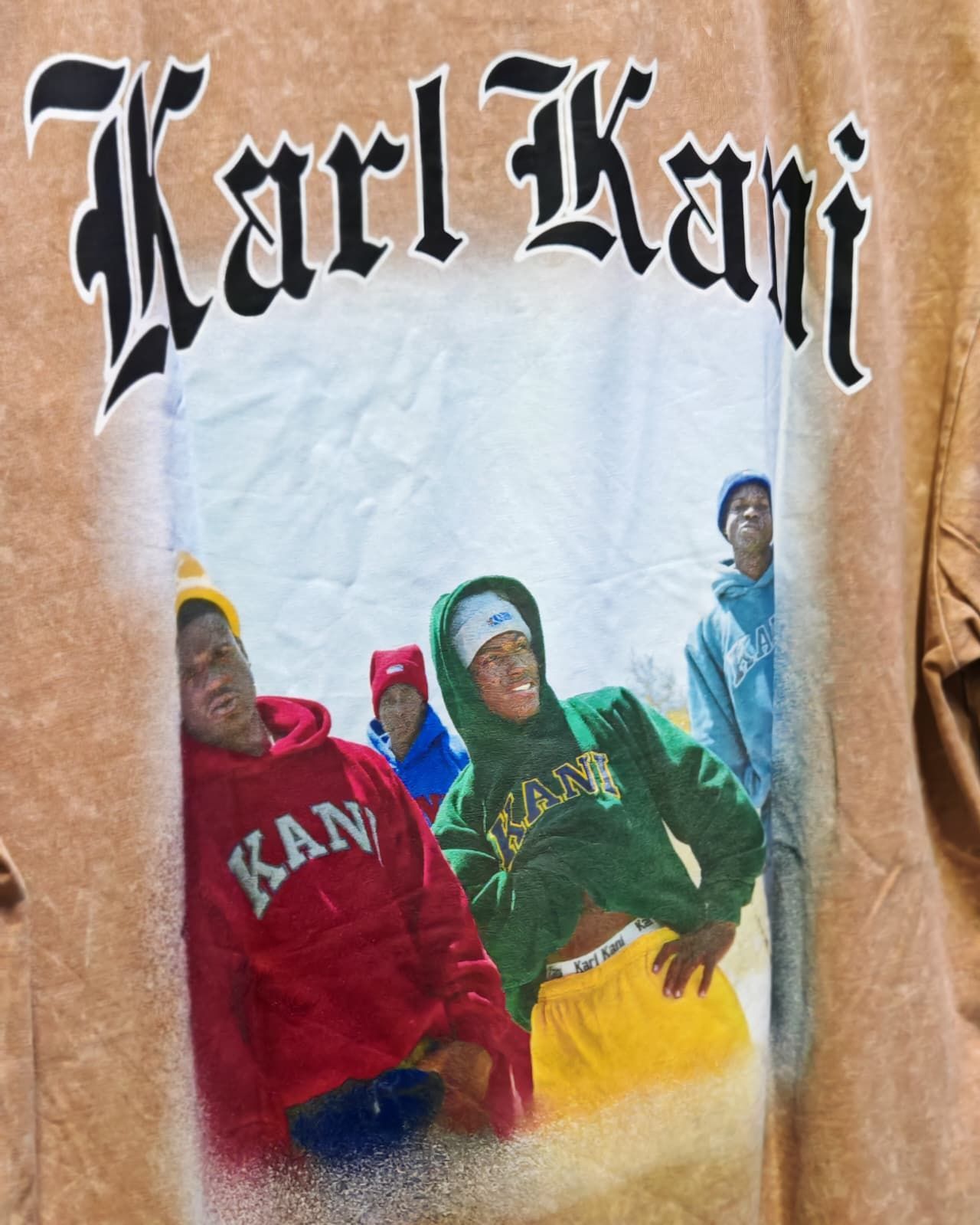 Il logo di Karl Kani sopra quattro persone con felpe colorate su un poster bianco stropicciato.