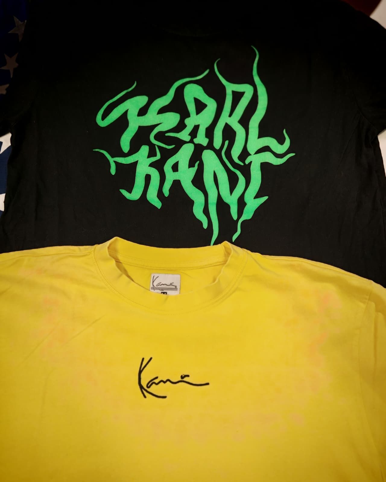 Due magliette sovrapposte: una nera con logo verde neon e una gialla con un piccolo logo nero in stile firma.