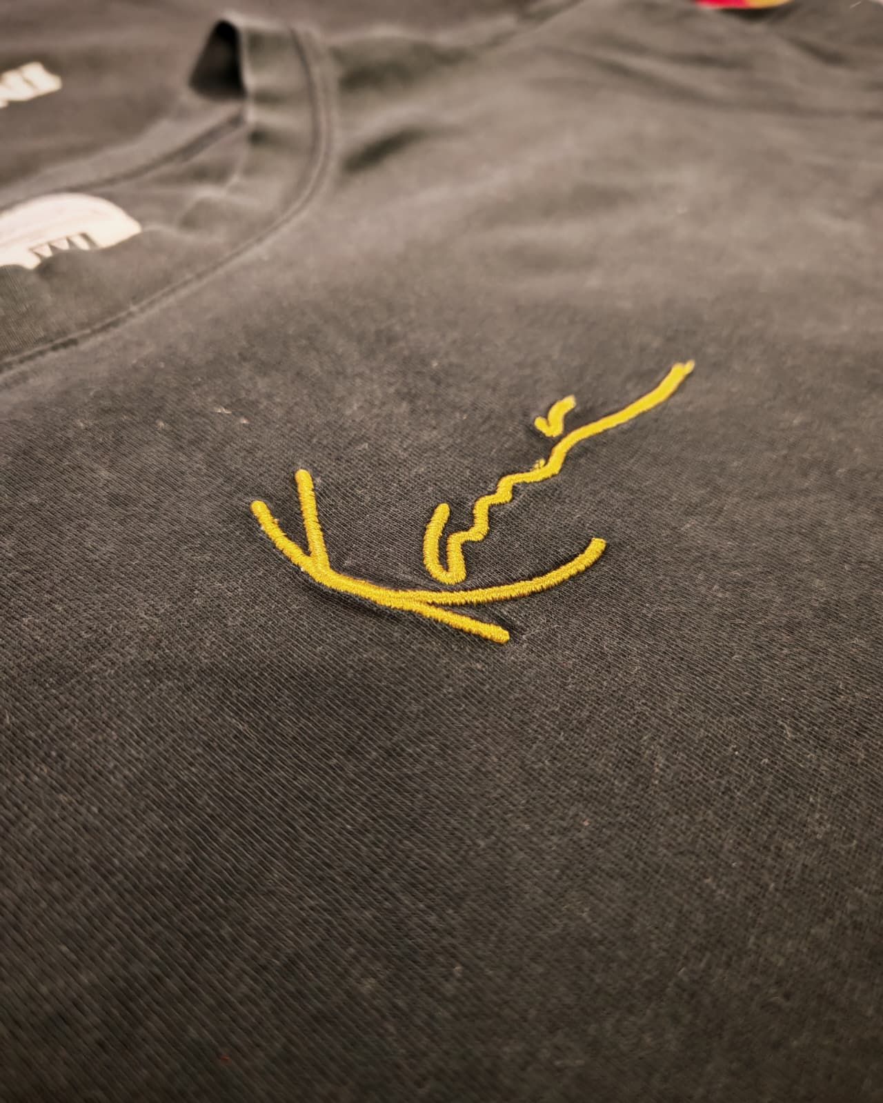 T-shirt nera con un piccolo ricamo giallo vicino al colletto.